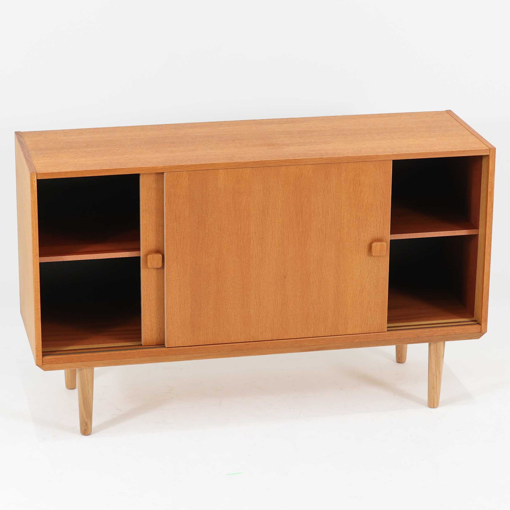 Domino Moblerが製作したデンマーク製ボードです。オーク材の明るく穏やかな木目を活かした端正なフレームです。引き戸構造により省スペースで使いやすく、内部には棚板を備え日用品や書類、食器などをすっきりと収納可能。幅122cmのバランスの取れたサイズ感で、リビングやダイニングのサイドキャビネットとしても活躍します。経年で味わいを増した木肌が空間に温もりと北欧ビンテージらしい趣を添える一品です。