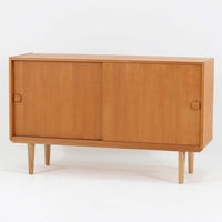 Domino Moblerが製作したデンマーク製ボードです。オーク材の明るく穏やかな木目を活かした端正なフレームです。引き戸構造により省スペースで使いやすく、内部には棚板を備え日用品や書類、食器などをすっきりと収納可能。幅122cmのバランスの取れたサイズ感で、リビングやダイニングのサイドキャビネットとしても活躍します。経年で味わいを増した木肌が空間に温もりと北欧ビンテージらしい趣を添える一品です。