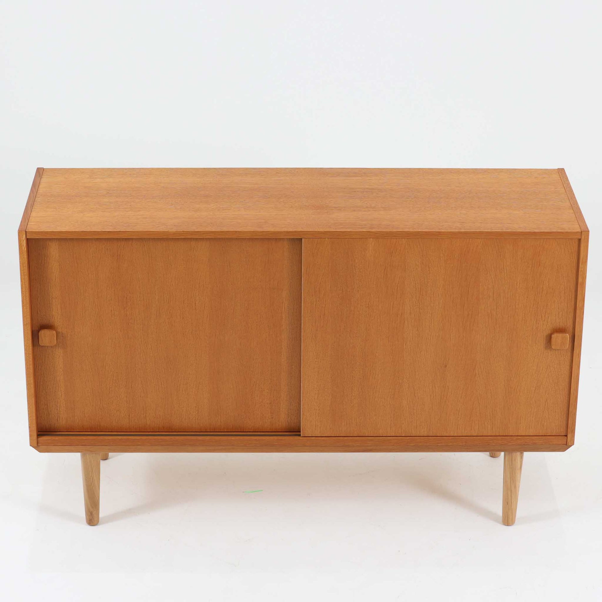 Domino Moblerが製作したデンマーク製ボードです。オーク材の明るく穏やかな木目を活かした端正なフレームです。引き戸構造により省スペースで使いやすく、内部には棚板を備え日用品や書類、食器などをすっきりと収納可能。幅122cmのバランスの取れたサイズ感で、リビングやダイニングのサイドキャビネットとしても活躍します。経年で味わいを増した木肌が空間に温もりと北欧ビンテージらしい趣を添える一品です。