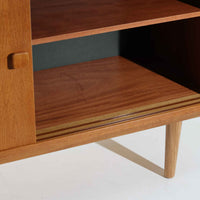 Domino Moblerが製作したデンマーク製ボードです。オーク材の明るく穏やかな木目を活かした端正なフレームです。引き戸構造により省スペースで使いやすく、内部には棚板を備え日用品や書類、食器などをすっきりと収納可能。幅122cmのバランスの取れたサイズ感で、リビングやダイニングのサイドキャビネットとしても活躍します。経年で味わいを増した木肌が空間に温もりと北欧ビンテージらしい趣を添える一品です。