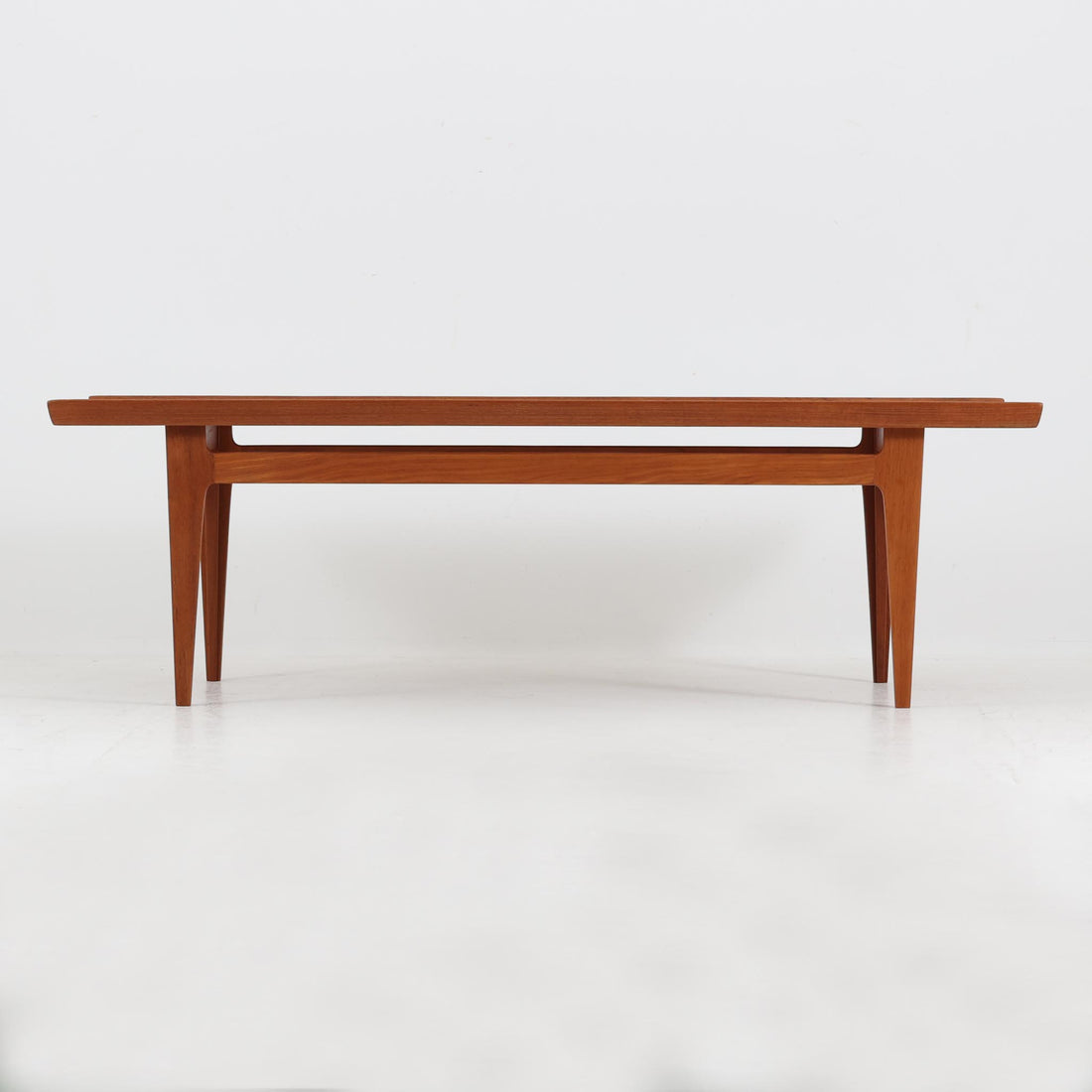 デンマークの名匠フィン・ユールによるデザイン、France & Son社製（前身のFrance & Daverkosen時代に製造）センターテーブル「FD532」です。1950～1957年頃の製造と推測され、チーク無垢材を贅沢に用いた質感豊かな仕上がりが魅力です。脚部から幕板にかけての有機的な曲線や彫刻的なフォルムはフィン・ユールならではの造形美を感じさせ、天板縁のわずかな立ち上がりが軽やかな印象を与えます。FD532には複数の高さバリエーションが存在しますが、本品は低めの約45cmモデルで、ソファ前に合わせやすいバランスの取れたサイズ感。北欧家具らしい温もりと職人技が融合した、希少かつ上質なビンテージテーブルです。