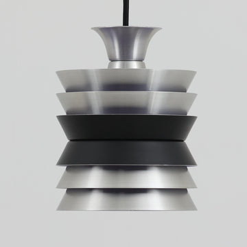 Carl ThoreがGranhaga Metallindustriで手掛けた直径15cmの小ぶりなペンダントライトで、段状に重ねたアルミシェードが光を柔らかく拡散し、点灯時には上下方向へ美しいグラデーションを生み出す北欧ビンテージ品です。繊細なヘアライン仕上げとブラックパーツのコントラストがモダンな印象を与え、キッチンカウンターや小空間のアクセント照明としてはもちろん、複数灯を並べたコーディネートにも最適です。コンパクトながら彫刻的なフォルムが存在感を放ち、経年で深まった質感がビンテージならではの魅力を際立たせています。