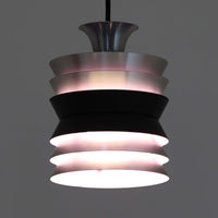 Carl ThoreがGranhaga Metallindustriで手掛けた直径15cmの小ぶりなペンダントライトで、段状に重ねたアルミシェードが光を柔らかく拡散し、点灯時には上下方向へ美しいグラデーションを生み出す北欧ビンテージ品です。繊細なヘアライン仕上げとブラックパーツのコントラストがモダンな印象を与え、キッチンカウンターや小空間のアクセント照明としてはもちろん、複数灯を並べたコーディネートにも最適です。コンパクトながら彫刻的なフォルムが存在感を放ち、経年で深まった質感がビンテージならではの魅力を際立たせています。