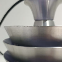 Carl ThoreがGranhaga Metallindustriで手掛けた直径15cmの小ぶりなペンダントライトで、段状に重ねたアルミシェードが光を柔らかく拡散し、点灯時には上下方向へ美しいグラデーションを生み出す北欧ビンテージ品です。繊細なヘアライン仕上げとブラックパーツのコントラストがモダンな印象を与え、キッチンカウンターや小空間のアクセント照明としてはもちろん、複数灯を並べたコーディネートにも最適です。コンパクトながら彫刻的なフォルムが存在感を放ち、経年で深まった質感がビンテージならではの魅力を際立たせています。