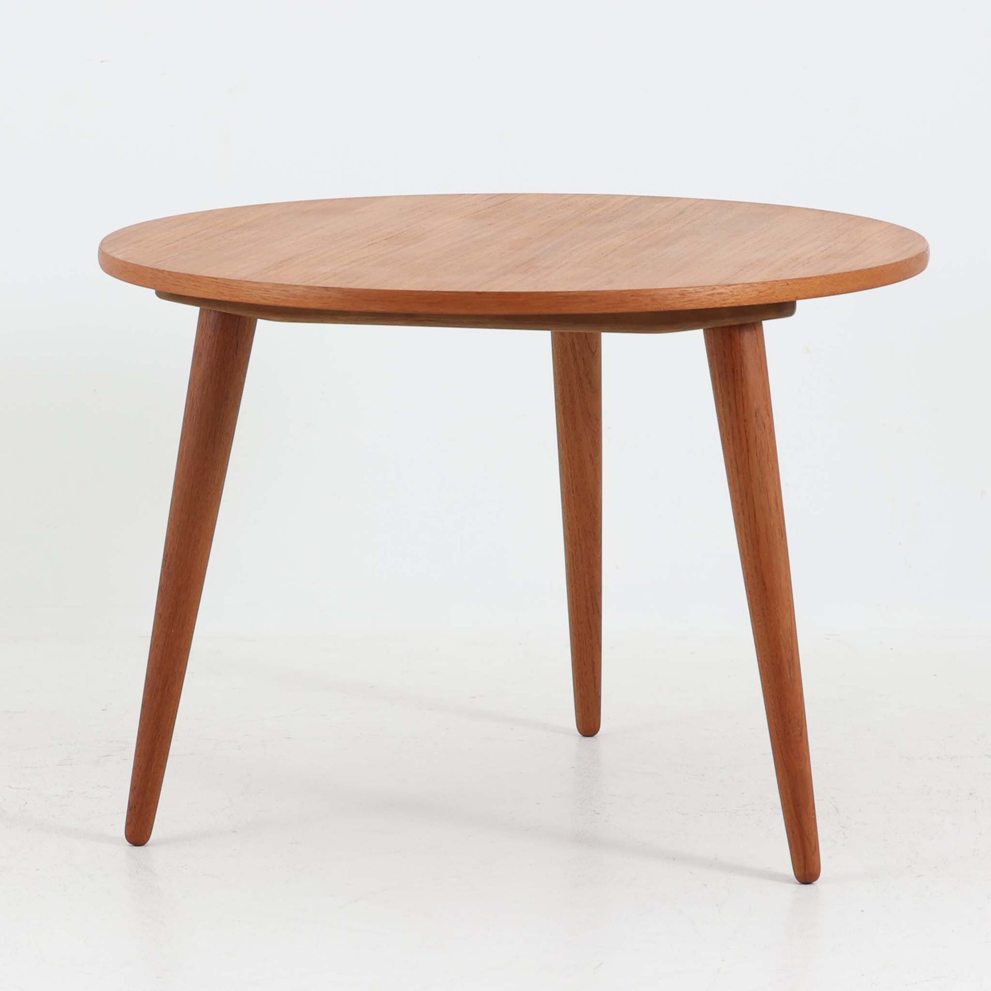 デンマークの巨匠Hans J. Wegner（ハンス・J・ウェグナー）がAndreas Tuck社のためにデザインした「AT8」円形センターテーブルです。チーク材による滑らかな天板と、3本脚の軽やかな構造が特徴で、美しくテーパーのついた脚部が全体に上品な印象を与えます。脚は木製のねじ込み構造になっており、工具を使わずに着脱が可能です。こうしたディテールにもビンテージ期ならではの職人技が感じられます。脚部までチーク材が使用された希少なタイプで、素材の統一感と温かみのある質感が際立ちます。ウェグナーらしいシンプルで機能的な造形と、経年により深みを増したチークの風合いが融合し、リビング空間に上質な北欧のぬくもりを添える一台です。
