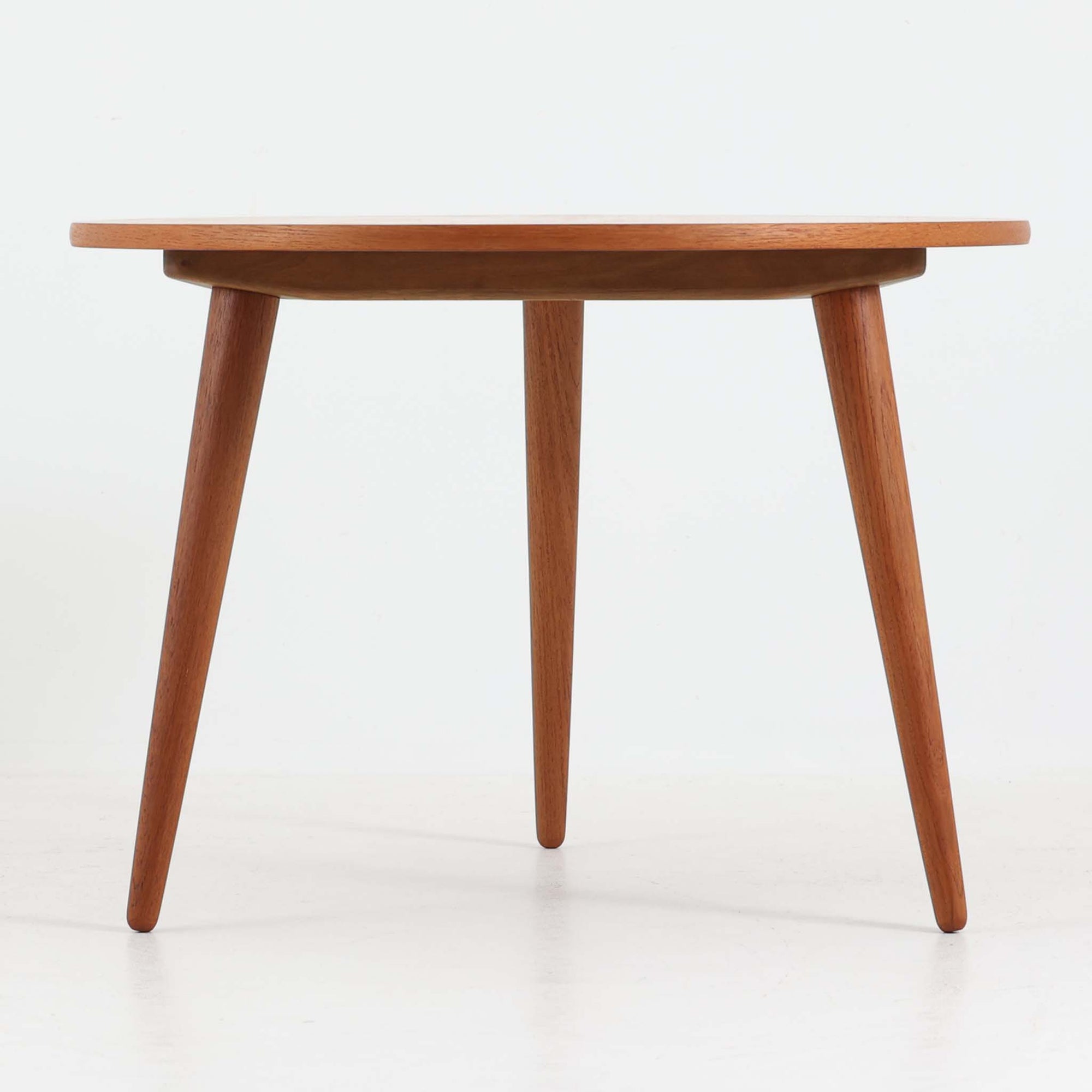 デンマークの巨匠Hans J. Wegner（ハンス・J・ウェグナー）がAndreas Tuck社のためにデザインした「AT8」円形センターテーブルです。チーク材による滑らかな天板と、3本脚の軽やかな構造が特徴で、美しくテーパーのついた脚部が全体に上品な印象を与えます。脚は木製のねじ込み構造になっており、工具を使わずに着脱が可能です。こうしたディテールにもビンテージ期ならではの職人技が感じられます。脚部までチーク材が使用された希少なタイプで、素材の統一感と温かみのある質感が際立ちます。ウェグナーらしいシンプルで機能的な造形と、経年により深みを増したチークの風合いが融合し、リビング空間に上質な北欧のぬくもりを添える一台です。