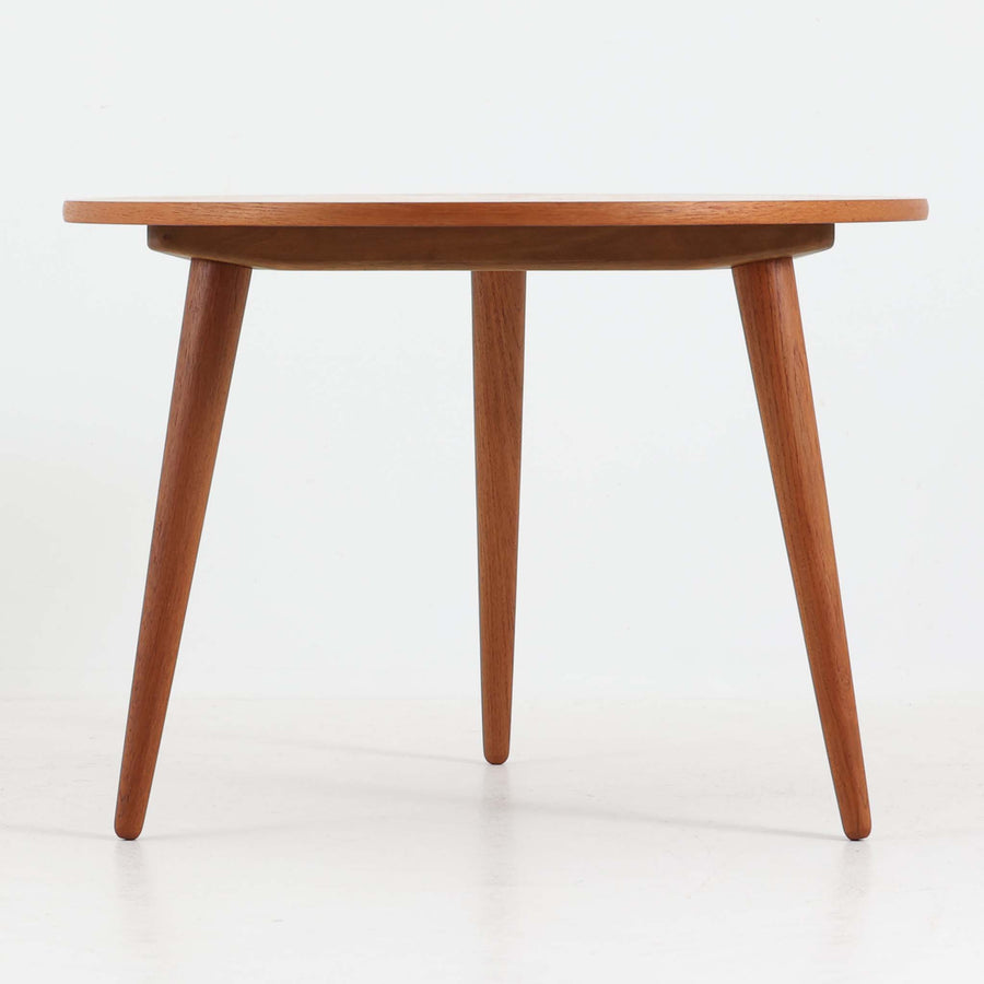 デンマークの巨匠Hans J. Wegner（ハンス・J・ウェグナー）がAndreas Tuck社のためにデザインした「AT8」円形センターテーブルです。チーク材による滑らかな天板と、3本脚の軽やかな構造が特徴で、美しくテーパーのついた脚部が全体に上品な印象を与えます。脚は木製のねじ込み構造になっており、工具を使わずに着脱が可能です。こうしたディテールにもビンテージ期ならではの職人技が感じられます。脚部までチーク材が使用された希少なタイプで、素材の統一感と温かみのある質感が際立ちます。ウェグナーらしいシンプルで機能的な造形と、経年により深みを増したチークの風合いが融合し、リビング空間に上質な北欧のぬくもりを添える一台です。