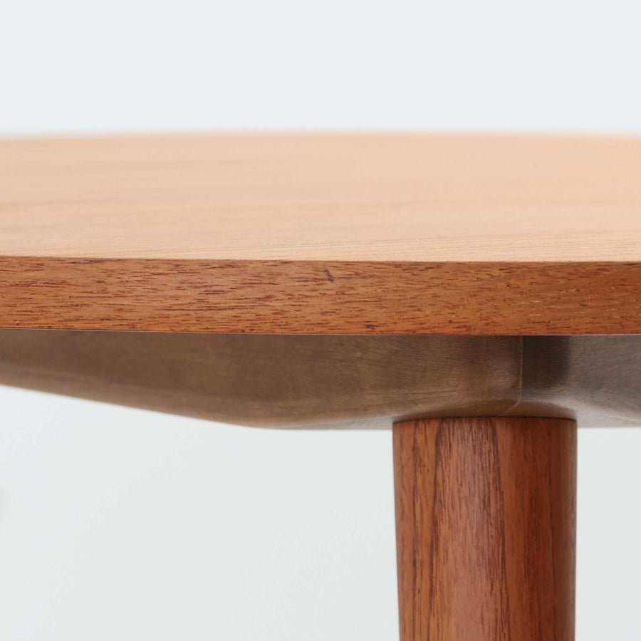 デンマークの巨匠Hans J. Wegner（ハンス・J・ウェグナー）がAndreas Tuck社のためにデザインした「AT8」円形センターテーブルです。チーク材による滑らかな天板と、3本脚の軽やかな構造が特徴で、美しくテーパーのついた脚部が全体に上品な印象を与えます。脚は木製のねじ込み構造になっており、工具を使わずに着脱が可能です。こうしたディテールにもビンテージ期ならではの職人技が感じられます。脚部までチーク材が使用された希少なタイプで、素材の統一感と温かみのある質感が際立ちます。ウェグナーらしいシンプルで機能的な造形と、経年により深みを増したチークの風合いが融合し、リビング空間に上質な北欧のぬくもりを添える一台です。