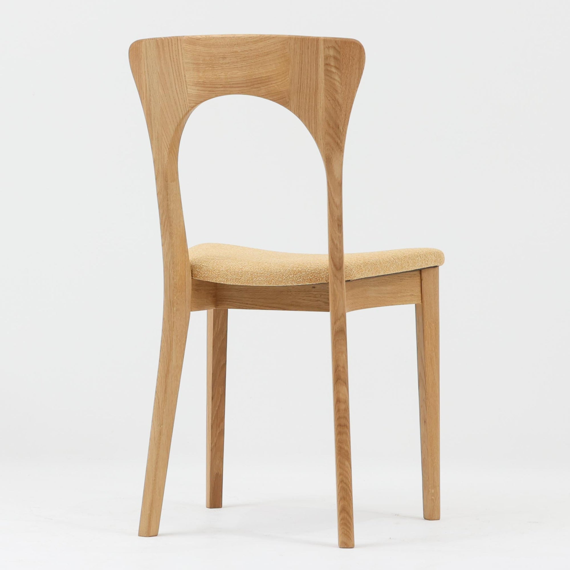 Niels Koefoedが1957年にデザインし、現在はCaso Furnitureより復刻製作されているモデル「Peter」のダイニングチェアです。オーク材の美しい木目を活かしたフレームと、背もたれに大きく設けられたアーチ状の開口部が印象的で、軽やかさと構造的な強度を両立したデザインが特徴です。身体をやさしく受け止める背のラインと、適度なクッション性を備えた座面により、日常使いにおいても快適な座り心地を実現しています。素材の質感を活かしたシンプルな佇まいは、ダイニング空間に自然と馴染み、北欧ミッドセンチュリー期のデザインらしい温かみと洗練を感じさせる一脚です。