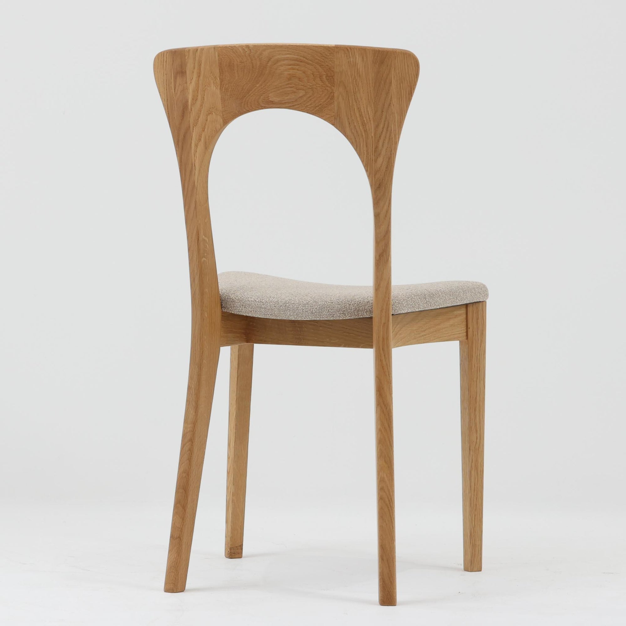 Niels Koefoedが1957年にデザインし、現在はCaso Furnitureより復刻製作されているモデル「Peter」のダイニングチェアです。オーク材の美しい木目を活かしたフレームと、背もたれに大きく設けられたアーチ状の開口部が印象的で、軽やかさと構造的な強度を両立したデザインが特徴です。身体をやさしく受け止める背のラインと、適度なクッション性を備えた座面により、日常使いにおいても快適な座り心地を実現しています。素材の質感を活かしたシンプルな佇まいは、ダイニング空間に自然と馴染み、北欧ミッドセンチュリー期のデザインらしい温かみと洗練を感じさせる一脚です。