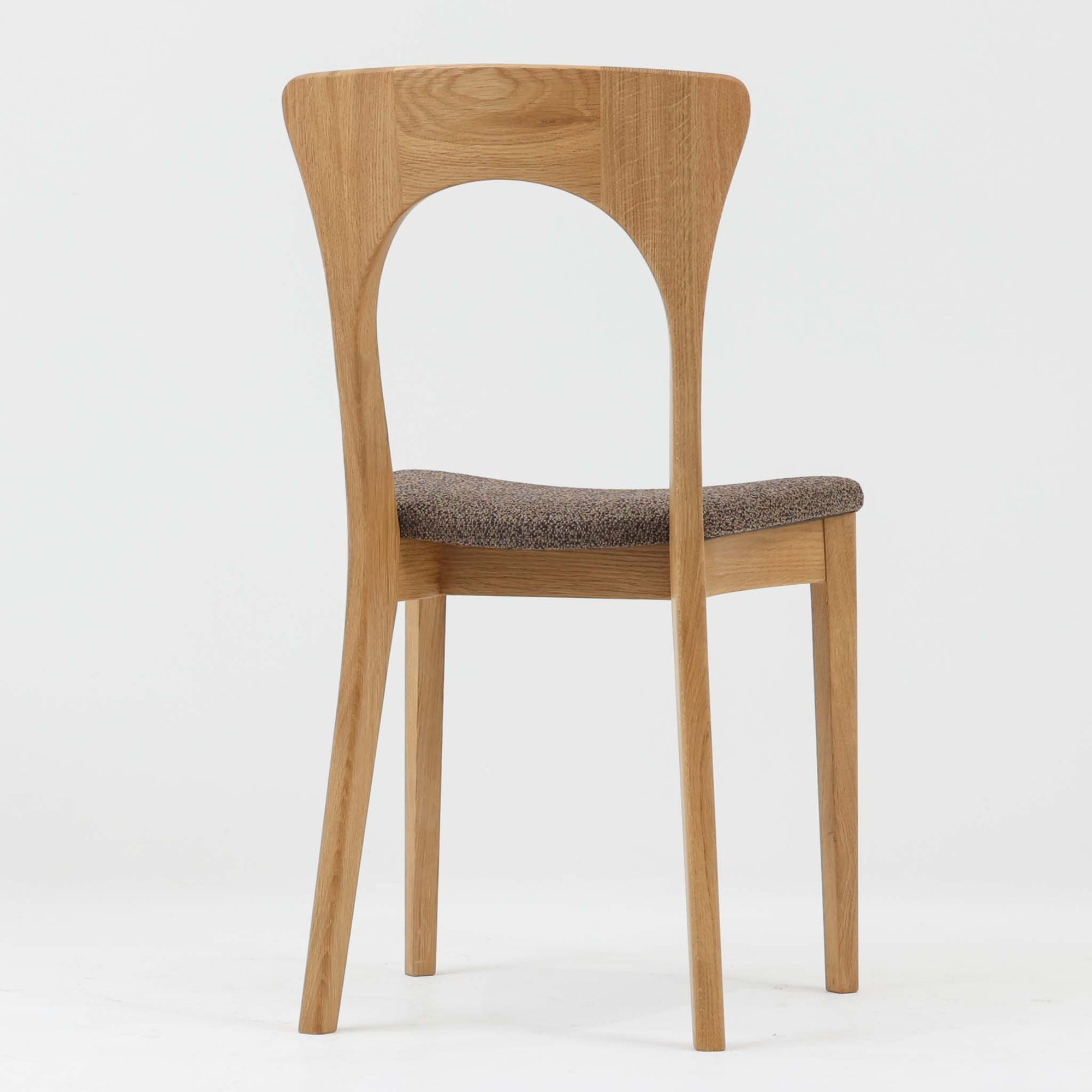 Niels Koefoedが1957年にデザインし、現在はCaso Furnitureより復刻製作されているモデル「Peter」のダイニングチェアです。オーク材の美しい木目を活かしたフレームと、背もたれに大きく設けられたアーチ状の開口部が印象的で、軽やかさと構造的な強度を両立したデザインが特徴です。身体をやさしく受け止める背のラインと、適度なクッション性を備えた座面により、日常使いにおいても快適な座り心地を実現しています。素材の質感を活かしたシンプルな佇まいは、ダイニング空間に自然と馴染み、北欧ミッドセンチュリー期のデザインらしい温かみと洗練を感じさせる一脚です。