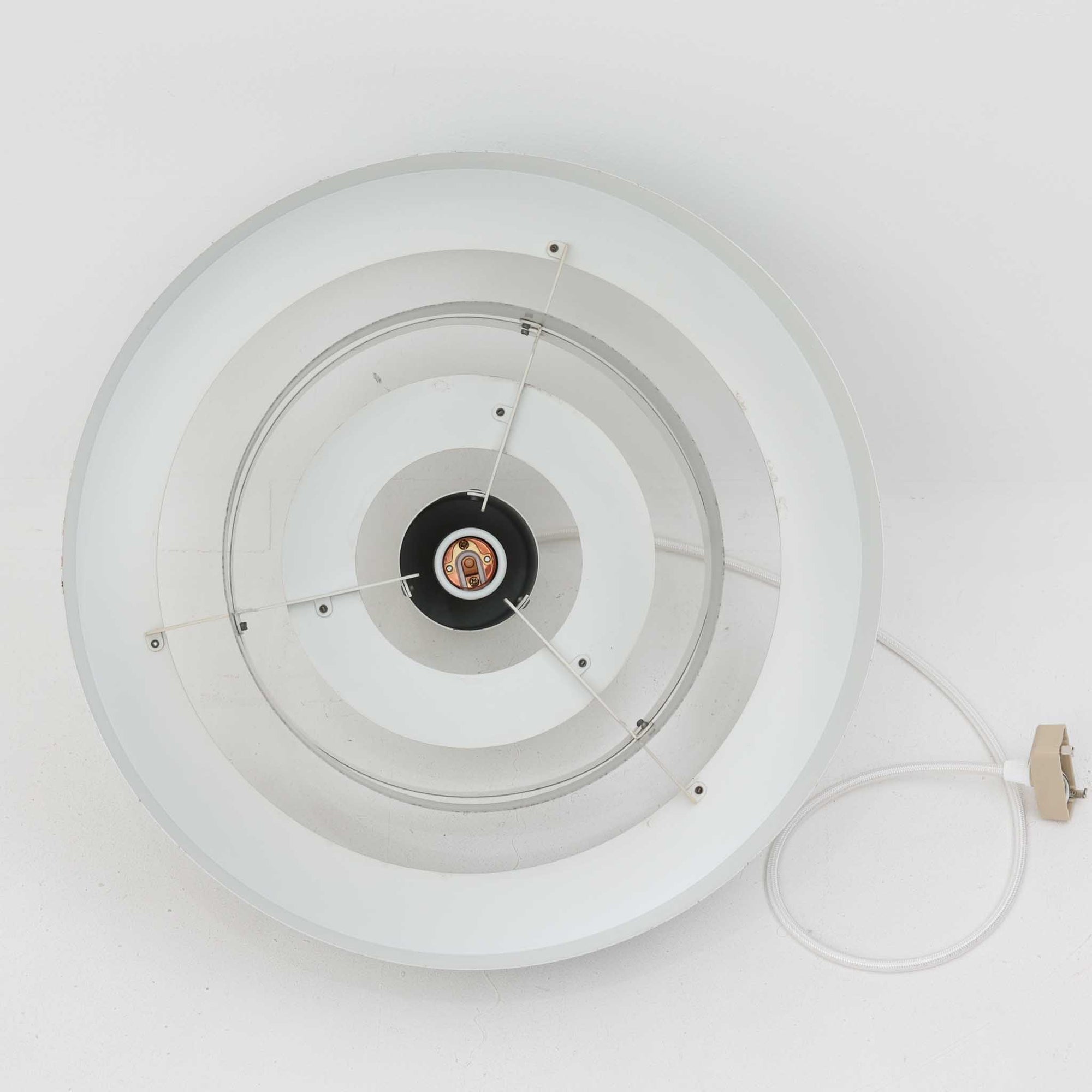 Jo HammerborgがFog &amp; Morupのためにデザインした「Equator」は、直径40cmの存在感あるスチール製ペンダントライトで、赤・黄色・青など多彩なカラーバリエーションが展開されていたモデルとして知られますが、本品は空間に優しく溶け込む上品なホワイトカラーが採用されています。スチール特有の程よい重量感と重厚な佇まいがあり、実際に吊るすとホワイトの柔らかな印象の中にしっかりとした質感が感じられるのも魅力です。同心円状に重なるシェードが光を柔らかく分散させ、眩しさを抑えつつ立体的な陰影を生み出す構造が特徴で、ダイニングやリビングの主照明として落ち着きのあるモダンなアクセントを添えます。ミニマルな造形の中に職人技が凝縮されており、経年で深まった塗装の質感がビンテージならではの魅力を一層引き立てています。