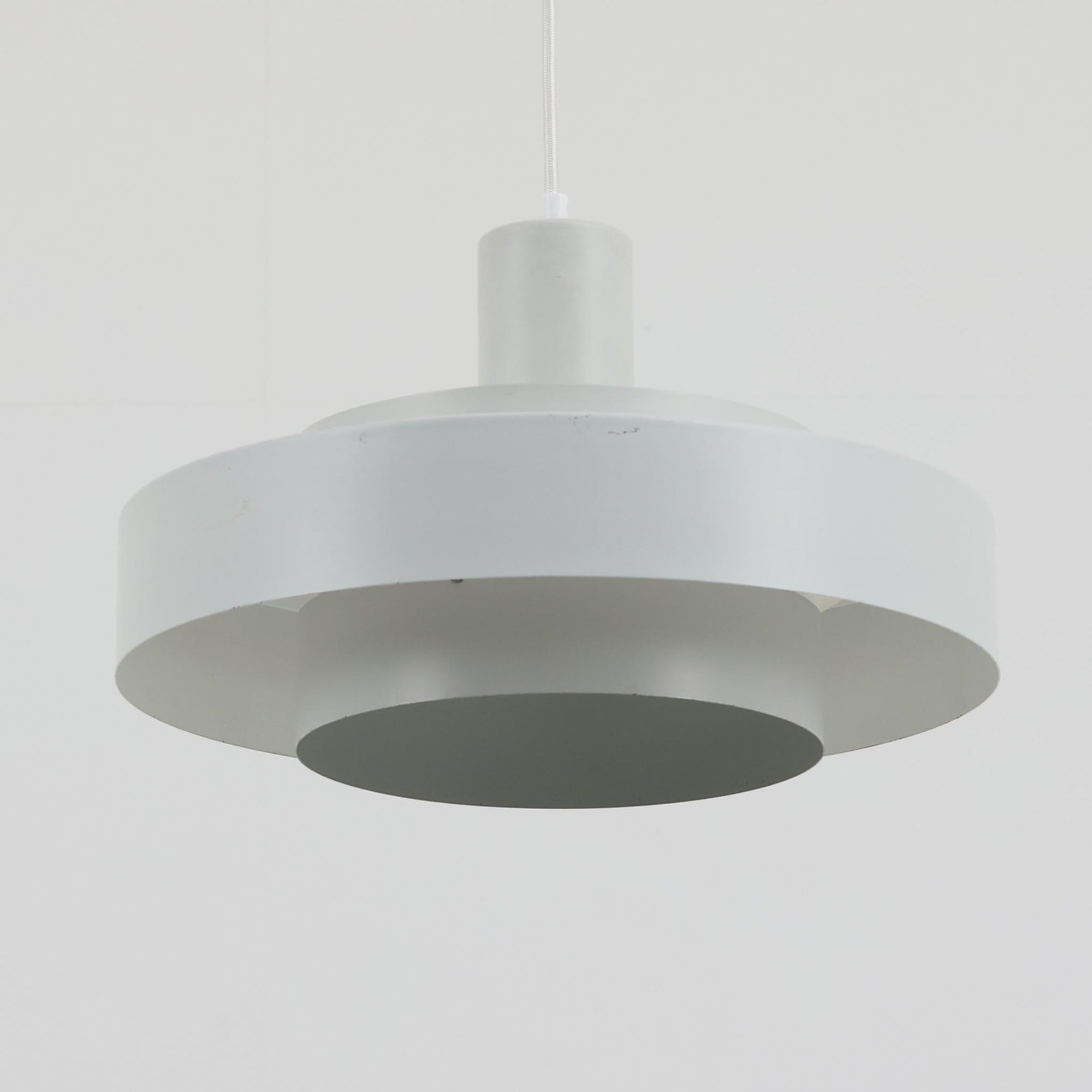 Jo HammerborgがFog &amp; Morupのためにデザインした「Equator」は、直径40cmの存在感あるスチール製ペンダントライトで、赤・黄色・青など多彩なカラーバリエーションが展開されていたモデルとして知られますが、本品は空間に優しく溶け込む上品なホワイトカラーが採用されています。スチール特有の程よい重量感と重厚な佇まいがあり、実際に吊るすとホワイトの柔らかな印象の中にしっかりとした質感が感じられるのも魅力です。同心円状に重なるシェードが光を柔らかく分散させ、眩しさを抑えつつ立体的な陰影を生み出す構造が特徴で、ダイニングやリビングの主照明として落ち着きのあるモダンなアクセントを添えます。ミニマルな造形の中に職人技が凝縮されており、経年で深まった塗装の質感がビンテージならではの魅力を一層引き立てています。