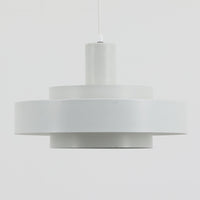 Jo HammerborgがFog & Morupのためにデザインした「Equator」は、直径40cmの存在感あるスチール製ペンダントライトで、赤・黄色・青など多彩なカラーバリエーションが展開されていたモデルとして知られますが、本品は空間に優しく溶け込む上品なホワイトカラーが採用されています。スチール特有の程よい重量感と重厚な佇まいがあり、実際に吊るすとホワイトの柔らかな印象の中にしっかりとした質感が感じられるのも魅力です。同心円状に重なるシェードが光を柔らかく分散させ、眩しさを抑えつつ立体的な陰影を生み出す構造が特徴で、ダイニングやリビングの主照明として落ち着きのあるモダンなアクセントを添えます。ミニマルな造形の中に職人技が凝縮されており、経年で深まった塗装の質感がビンテージならではの魅力を一層引き立てています。