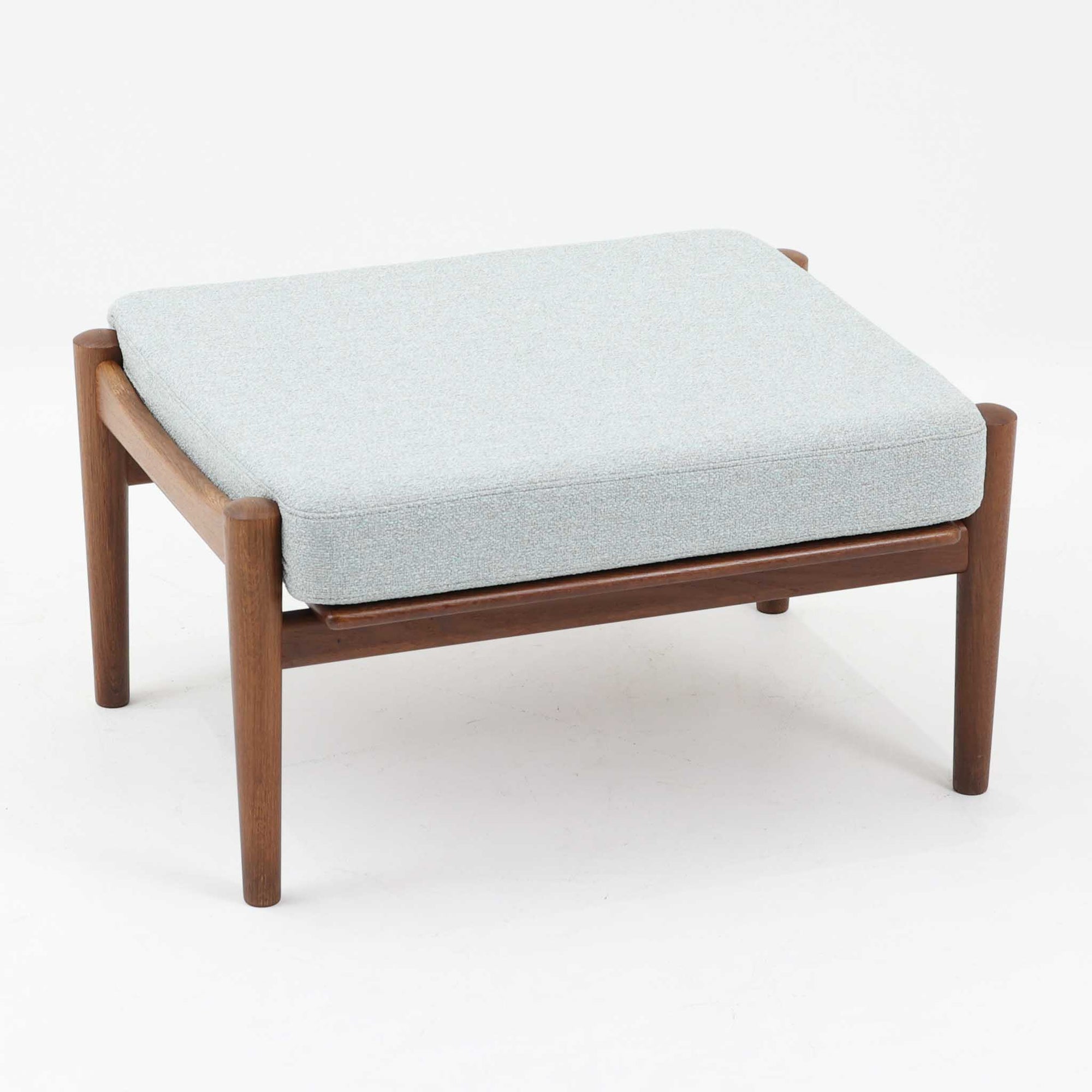 Hans J. Wegnerがデザインし、Getamaが製作したGE530オットマンです。ダークオーク材の力強い木目を活かした角の取れたフレームと、丸脚を組み合わせた端正な構造が特徴で、裏面には刻印も確認できます。程よい厚みのクッションは張り替え済みで、軽やかな生地が木部の深みのある色合いを引き立てます。同シリーズのラウンジチェアと合わせてはもちろん、単体でスツールや補助椅子としても活躍する、北欧ビンテージならではの質実剛健な一品です。