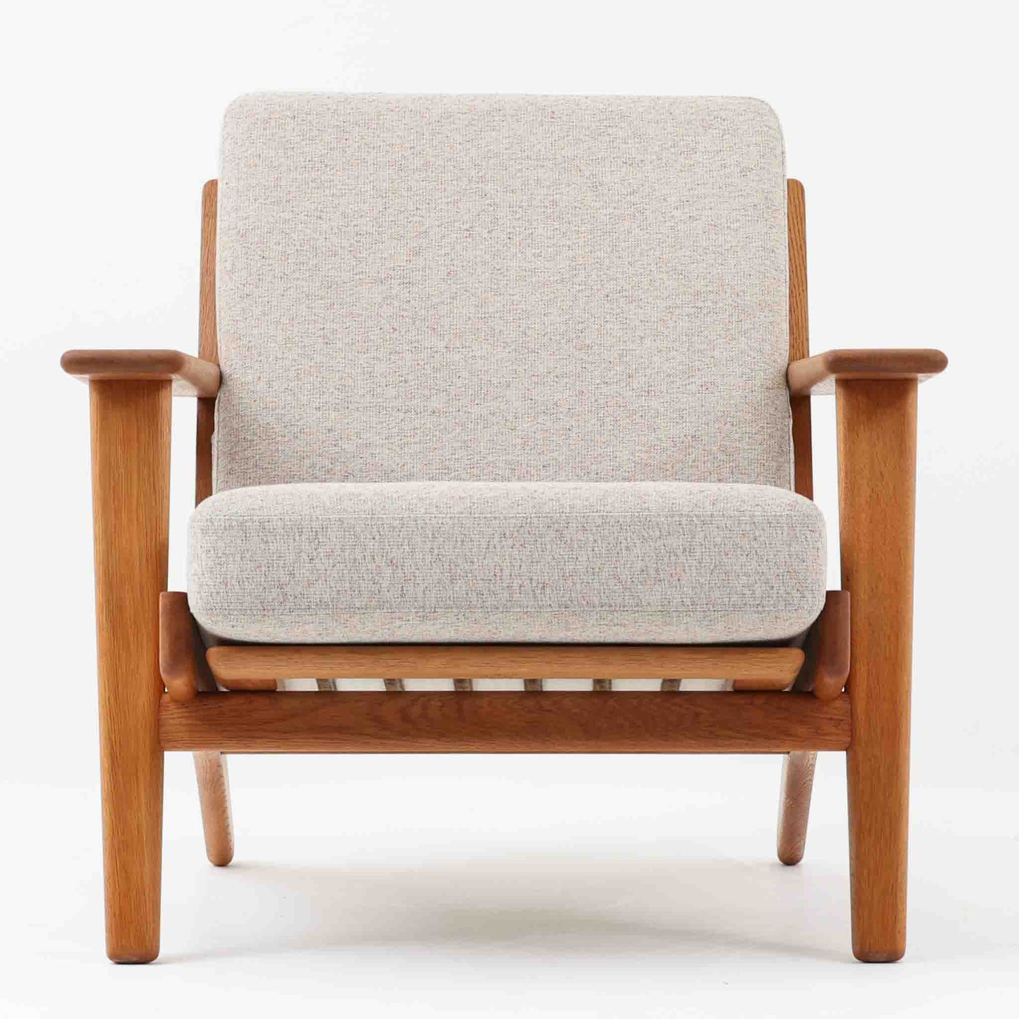 Hans J. Wegnerがデザインし、Getama社によって製作されたGE290は、構造の美しさと快適な座り心地を兼ね備えた北欧ビンテージを代表するシングルソファです。厚みのあるクッションと緩やかに傾斜した背もたれが身体を包み込み、自然と深いリラックス姿勢へと導きます。クッション内部にはビンテージ品ならではのスプリングが内包されており、しっかりとした弾力と安定感のある座り心地を生み出しています。オーク材のフレームは力強さと温かみを併せ持ち、アームから脚部にかけての造形にはウェグナーらしい彫刻的な魅力が感じられます。張地の落ち着いた色合いと、経年により深みを増した木部の表情が調和し、リビングや書斎で長く寄り添う一脚です。