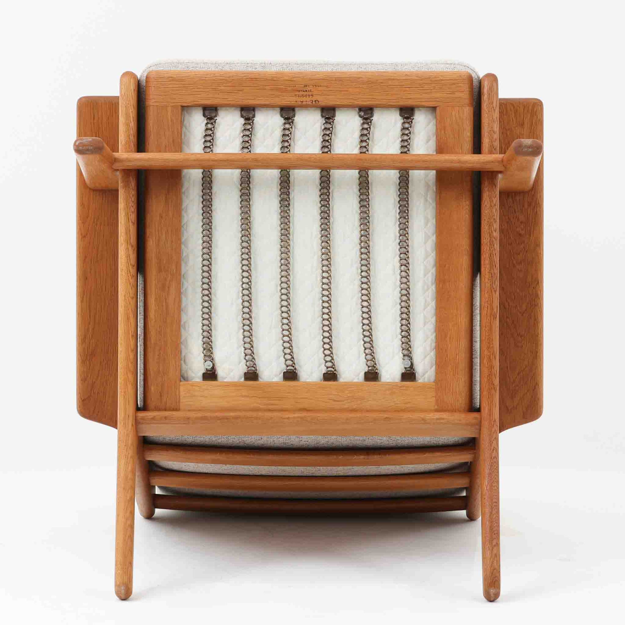 Hans J. Wegnerがデザインし、Getama社によって製作されたGE290は、構造の美しさと快適な座り心地を兼ね備えた北欧ビンテージを代表するシングルソファです。厚みのあるクッションと緩やかに傾斜した背もたれが身体を包み込み、自然と深いリラックス姿勢へと導きます。クッション内部にはビンテージ品ならではのスプリングが内包されており、しっかりとした弾力と安定感のある座り心地を生み出しています。オーク材のフレームは力強さと温かみを併せ持ち、アームから脚部にかけての造形にはウェグナーらしい彫刻的な魅力が感じられます。張地の落ち着いた色合いと、経年により深みを増した木部の表情が調和し、リビングや書斎で長く寄り添う一脚です。