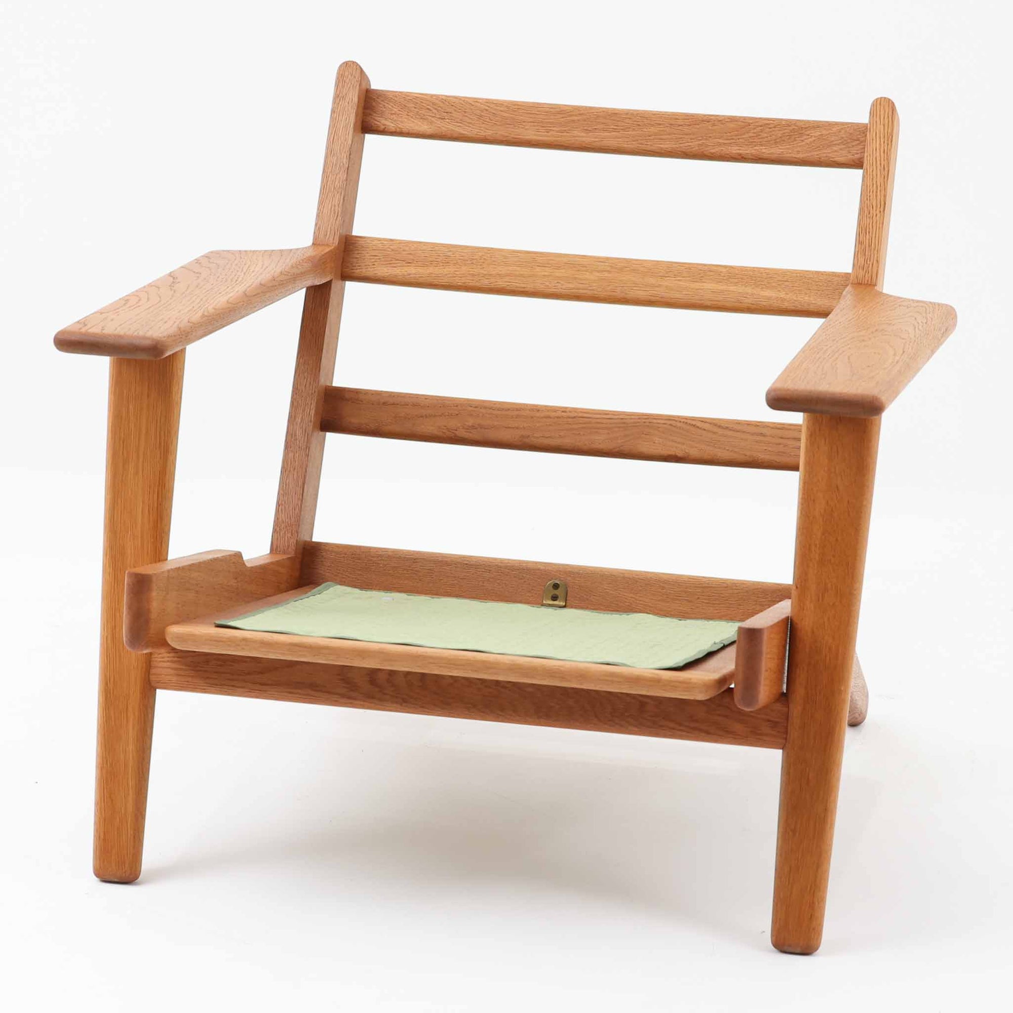 Hans J. Wegnerがデザインし、Getama社によって製作されたGE290は、構造の美しさと快適な座り心地を兼ね備えた北欧ビンテージを代表するシングルソファです。厚みのあるクッションと緩やかに傾斜した背もたれが身体を包み込み、自然と深いリラックス姿勢へと導きます。クッション内部にはビンテージ品ならではのスプリングが内包されており、しっかりとした弾力と安定感のある座り心地を生み出しています。オーク材のフレームは力強さと温かみを併せ持ち、アームから脚部にかけての造形にはウェグナーらしい彫刻的な魅力が感じられます。張地の落ち着いた色合いと、経年により深みを増した木部の表情が調和し、リビングや書斎で長く寄り添う一脚です。