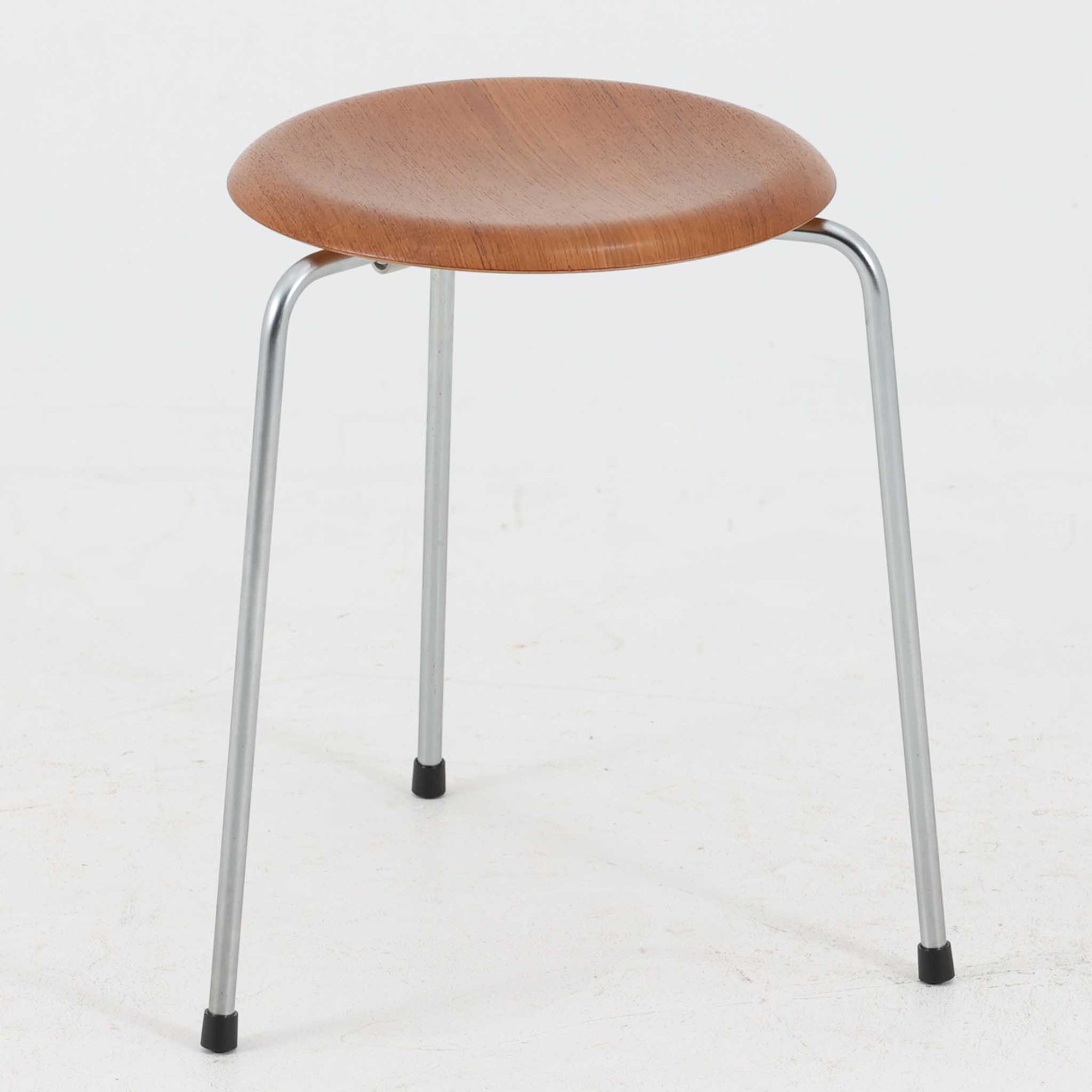 Arne Jacobsen（アルネ・ヤコブセン）がFritz Hansen（フリッツ・ハンセン）のために手掛けた有名なドットスツールは、チーク材の座面とスチールレッグを組み合わせた軽快な佇まいが魅力の北欧ビンテージ家具で、中でも希少なチークモデルとなるこちらは滑らかに成形された丸い座面が身体に心地よくフィットし、わずかに外側へ開いた3本脚が安定感を確保しつつ空間に軽やかな印象を添え、ミニマルな構造に宿る職人技と経年で深まった木肌と金属のコントラストが美しく、ダイニングのサブチェアや玄関、デスク横のサイドスツールとしても取り入れやすい一脚です。