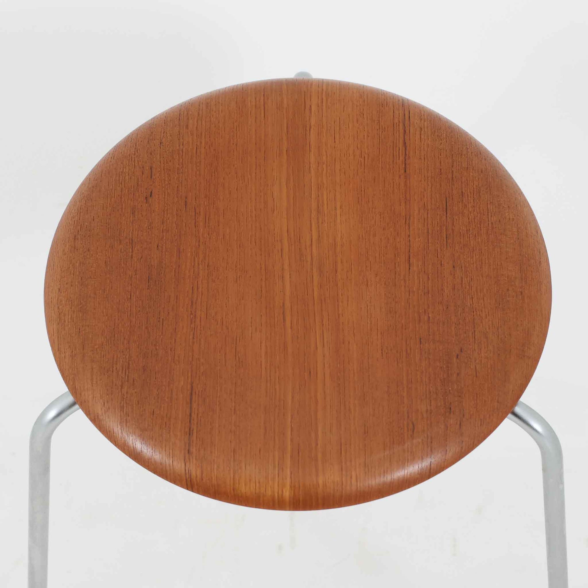 Arne Jacobsen（アルネ・ヤコブセン）がFritz Hansen（フリッツ・ハンセン）のために手掛けた有名なドットスツールは、チーク材の座面とスチールレッグを組み合わせた軽快な佇まいが魅力の北欧ビンテージ家具で、中でも希少なチークモデルとなるこちらは滑らかに成形された丸い座面が身体に心地よくフィットし、わずかに外側へ開いた3本脚が安定感を確保しつつ空間に軽やかな印象を添え、ミニマルな構造に宿る職人技と経年で深まった木肌と金属のコントラストが美しく、ダイニングのサブチェアや玄関、デスク横のサイドスツールとしても取り入れやすい一脚です。