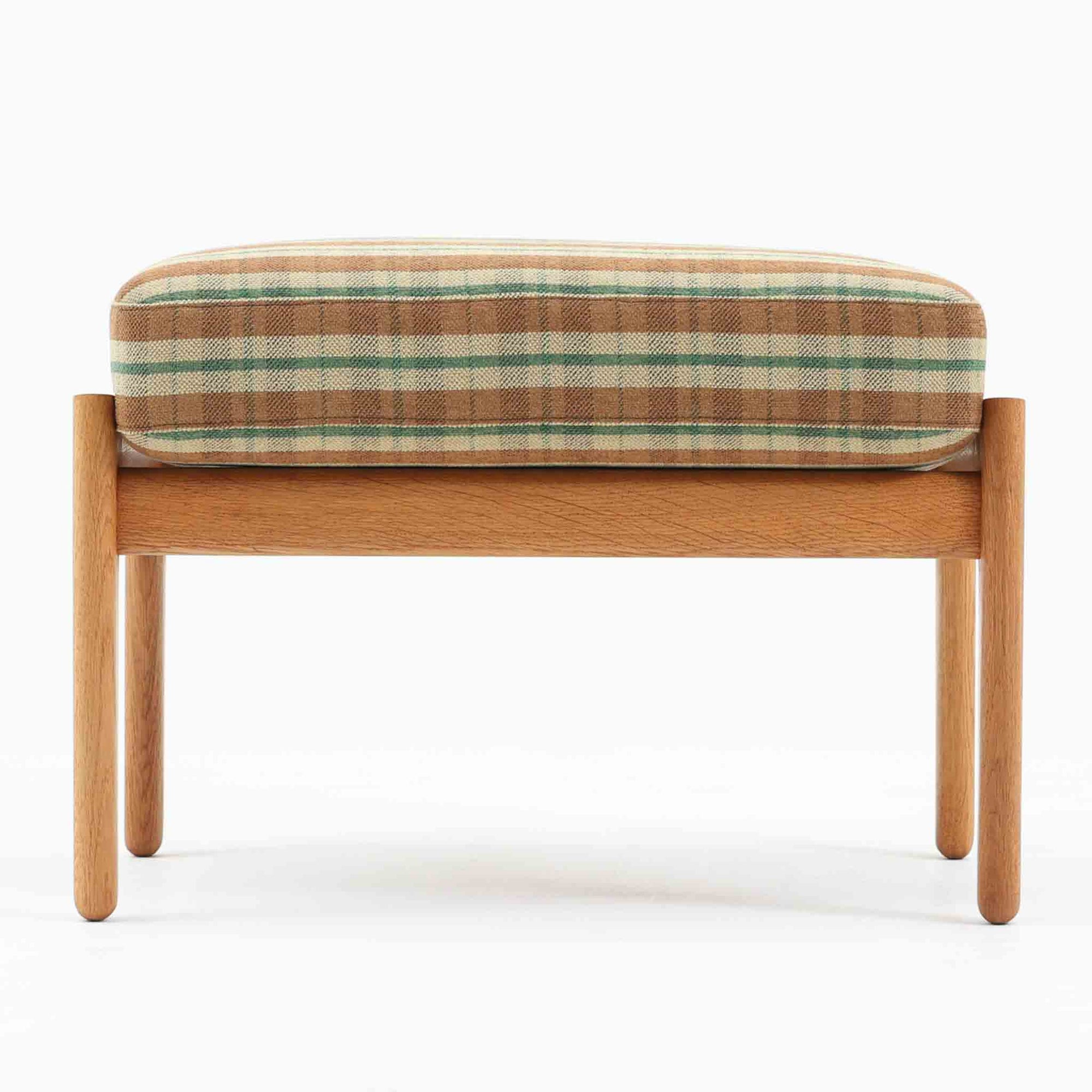 Hans J. Wegnerがデザインし、Getamaが製作したGE290オットマンです。オーク材の美しい木目を活かした無垢フレームは、丸みを帯びた脚部と貫構造により安定感と軽やかさを兼ね備えています。クッションは張り替え済みで、落ち着いたストライプ柄が木部の温かな色合いを引き立てます。同シリーズのラウンジチェアと組み合わせて快適な寛ぎを演出するのはもちろん、単体でもスツールとして活躍。経年で深みを増した素材感が、北欧ビンテージならではの上質な存在感を放つ一品です。クッション内部にはビンテージ品ならではのスプリングが内包されています。