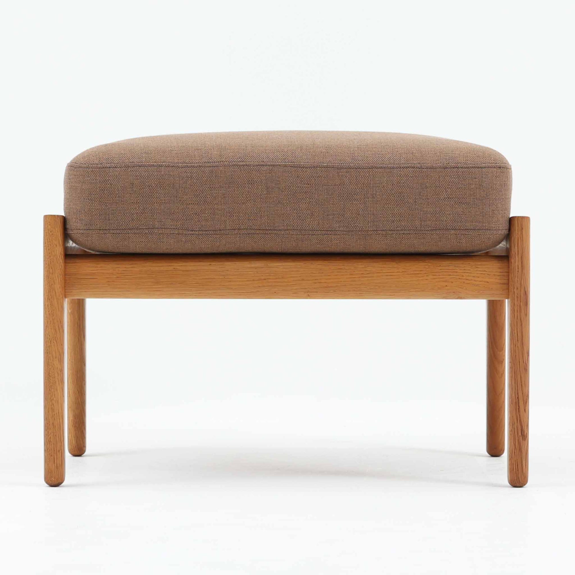 Hans J. Wegnerがデザインし、Getamaが製作したGE290オットマンです。オーク材の美しい木目を活かした無垢フレームは、丸みを帯びた脚部と貫構造により安定感と軽やかさを兼ね備えています。クッションは張り替え済みで、ライトブラウン色の張地が木部の温かな色合いと調和し、落ち着いた印象を与えます。内部にはビンテージ品ならではのスプリングが内包され、弾力ある座り心地も魅力。同シリーズのラウンジチェアと組み合わせてはもちろん、単体でもスツールとして活躍する、経年変化の味わい深い一品です。