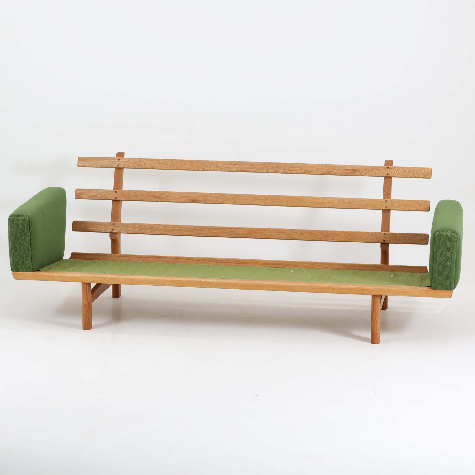 Hans J. Wegnerがデザインし、Getamaより製作されたGE236トリプルソファです。オーク材のフレームと直線を基調とした端正なフォルムが美しく、背面に配された横桟の意匠は後ろ姿まで印象的に演出します。ゆったりとした3人掛けの座面とクッションは快適な座り心地を実現し、リビングの主役として存在感を放ちます。ウェグナーらしい機能美と職人技が息づく設計に加え、経年により深みを増した木肌の風合いが北欧ビンテージならではの魅力を引き立てる希少な一台です。