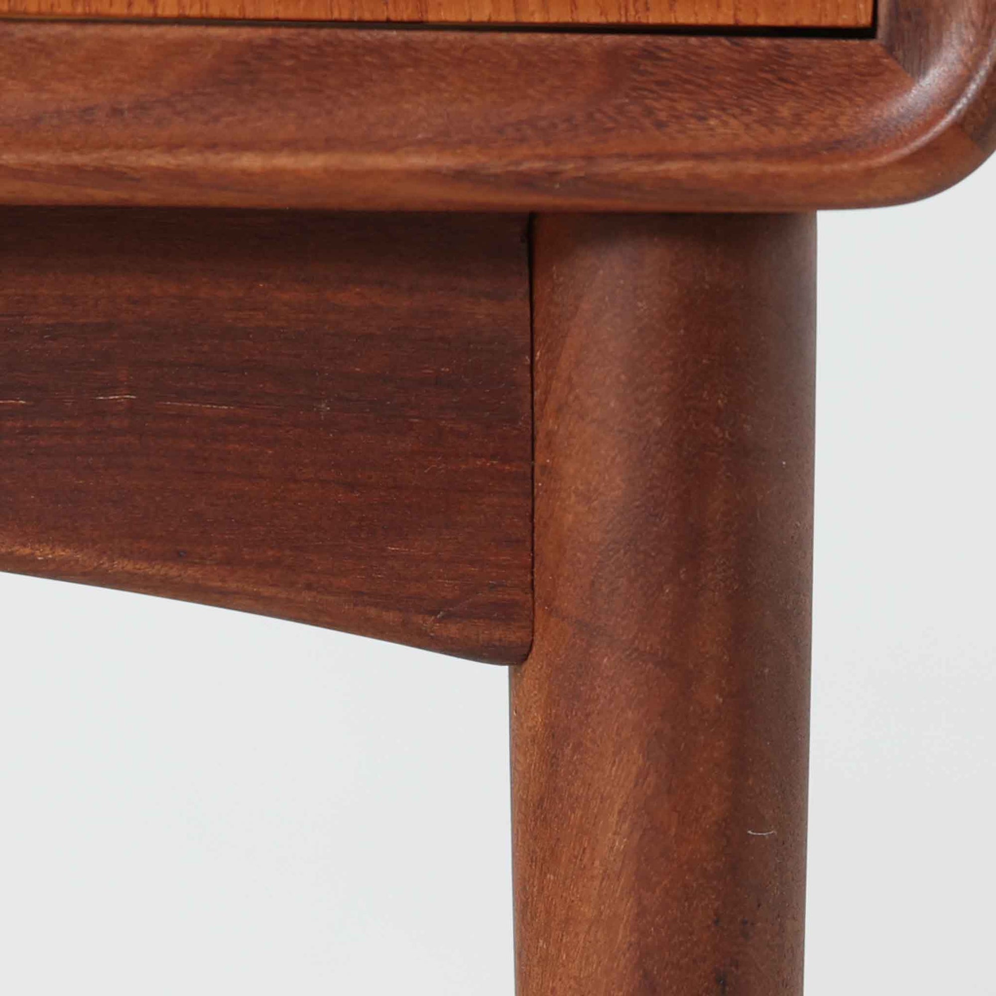 Johannes Andersen（ヨハネス・アンダーセン）がCFC Silkeborgのために手掛けた2段チェストは、チーク材を贅沢に用いた柔らかな曲面フォルムと長く伸びた彫刻的なハンドルが印象的で、天板から側面へと美しくつながる木目が上質な素材感を際立たせる北欧ビンテージ家具です。職人技の光る滑らかな面取りや端正な造りが深い味わいを生み出し、コンパクトながら実用的な2杯の引き出しを備え、ベッドサイドやリビングのサイドテーブルとしても活躍し、温かみのある木肌の経年変化が魅力を一層引き立てています。