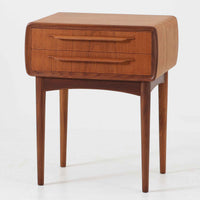 Johannes Andersen（ヨハネス・アンダーセン）がCFC Silkeborgのために手掛けた2段チェストは、チーク材を贅沢に用いた柔らかな曲面フォルムと長く伸びた彫刻的なハンドルが印象的で、天板から側面へと美しくつながる木目が上質な素材感を際立たせる北欧ビンテージ家具です。職人技の光る滑らかな面取りや端正な造りが深い味わいを生み出し、コンパクトながら実用的な2杯の引き出しを備え、ベッドサイドやリビングのサイドテーブルとしても活躍し、温かみのある木肌の経年変化が魅力を一層引き立てています。