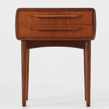 Johannes Andersen（ヨハネス・アンダーセン）がCFC Silkeborgのために手掛けた2段チェストは、チーク材を贅沢に用いた柔らかな曲面フォルムと長く伸びた彫刻的なハンドルが印象的で、天板から側面へと美しくつながる木目が上質な素材感を際立たせる北欧ビンテージ家具です。職人技の光る滑らかな面取りや端正な造りが深い味わいを生み出し、コンパクトながら実用的な2杯の引き出しを備え、ベッドサイドやリビングのサイドテーブルとしても活躍し、温かみのある木肌の経年変化が魅力を一層引き立てています。