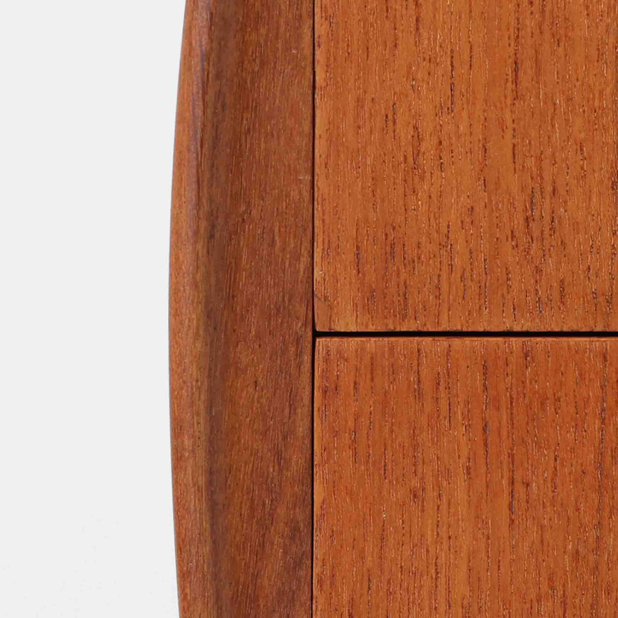 Johannes Andersen（ヨハネス・アンダーセン）がCFC Silkeborgのために手掛けた2段チェストは、チーク材を贅沢に用いた柔らかな曲面フォルムと長く伸びた彫刻的なハンドルが印象的で、天板から側面へと美しくつながる木目が上質な素材感を際立たせる北欧ビンテージ家具です。職人技の光る滑らかな面取りや端正な造りが深い味わいを生み出し、コンパクトながら実用的な2杯の引き出しを備え、ベッドサイドやリビングのサイドテーブルとしても活躍し、温かみのある木肌の経年変化が魅力を一層引き立てています。