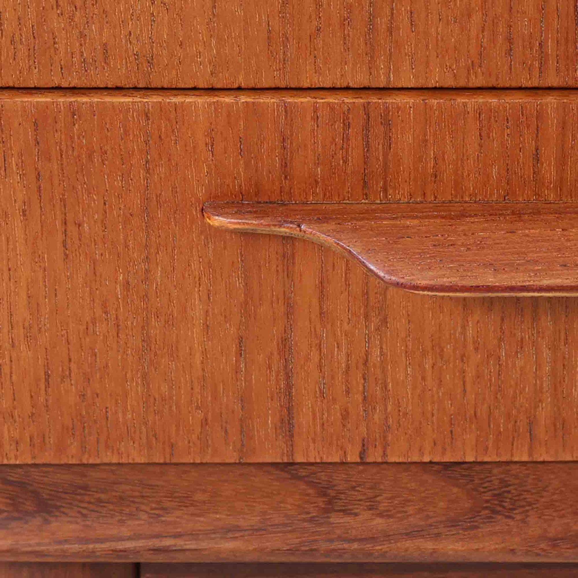 Johannes Andersen（ヨハネス・アンダーセン）がCFC Silkeborgのために手掛けた2段チェストは、チーク材を贅沢に用いた柔らかな曲面フォルムと長く伸びた彫刻的なハンドルが印象的で、天板から側面へと美しくつながる木目が上質な素材感を際立たせる北欧ビンテージ家具です。職人技の光る滑らかな面取りや端正な造りが深い味わいを生み出し、コンパクトながら実用的な2杯の引き出しを備え、ベッドサイドやリビングのサイドテーブルとしても活躍し、温かみのある木肌の経年変化が魅力を一層引き立てています。