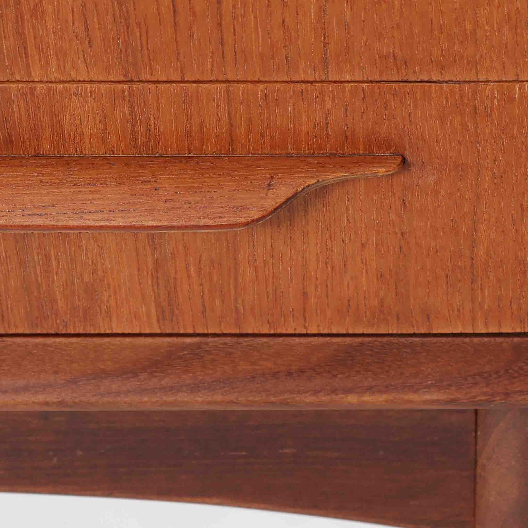 Johannes Andersen（ヨハネス・アンダーセン）がCFC Silkeborgのために手掛けた2段チェストは、チーク材を贅沢に用いた柔らかな曲面フォルムと長く伸びた彫刻的なハンドルが印象的で、天板から側面へと美しくつながる木目が上質な素材感を際立たせる北欧ビンテージ家具です。職人技の光る滑らかな面取りや端正な造りが深い味わいを生み出し、コンパクトながら実用的な2杯の引き出しを備え、ベッドサイドやリビングのサイドテーブルとしても活躍し、温かみのある木肌の経年変化が魅力を一層引き立てています。