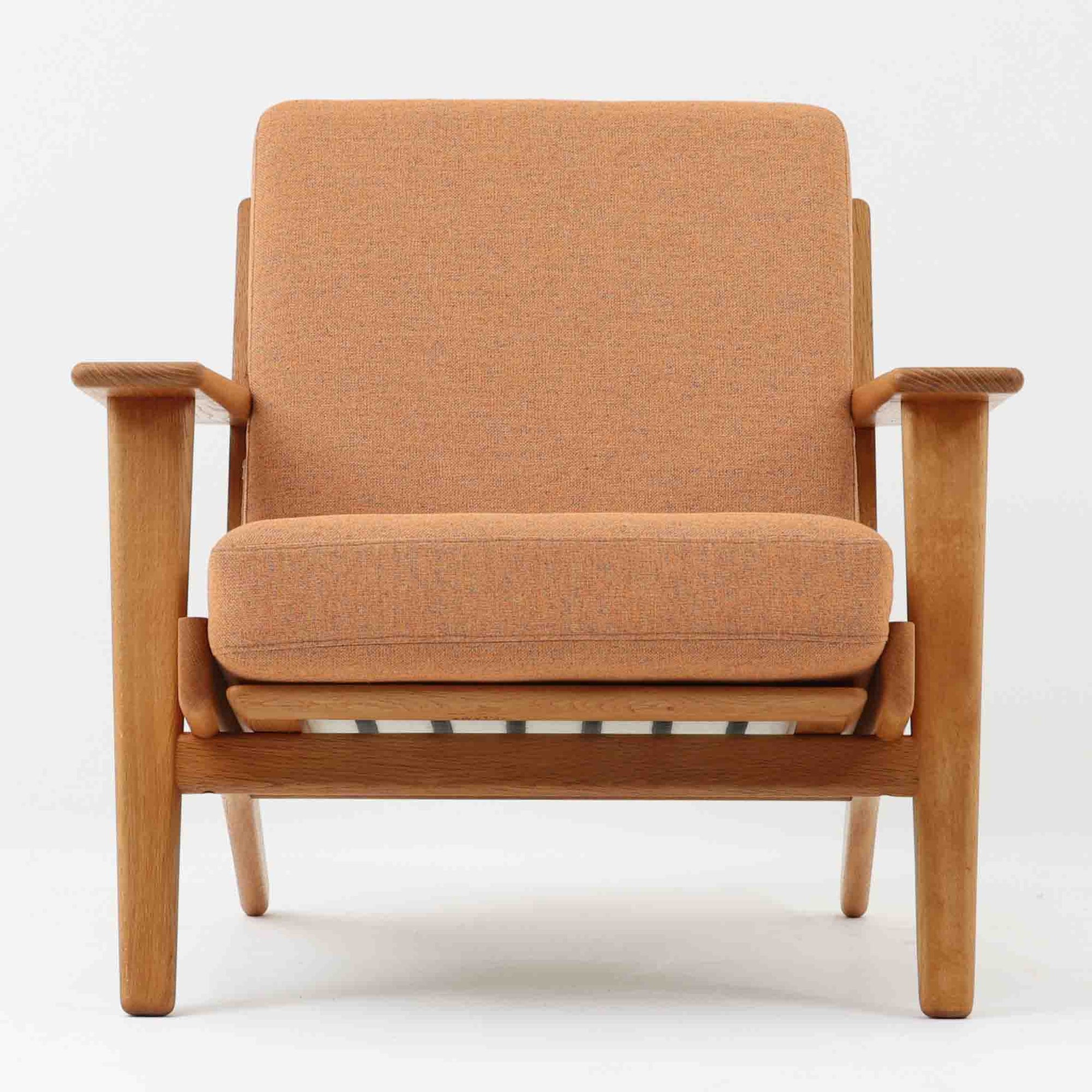 Hans J. Wegnerがデザインし、Getama社によって製作されたGE290は、構造の美しさと快適な座り心地を兼ね備えた北欧ビンテージを代表するシングルソファです。厚みのあるクッションと緩やかに傾斜した背もたれが身体を包み込み、自然と深いリラックス姿勢へと導きます。クッション内部にはビンテージ品ならではのスプリングが内包されており、しっかりとした弾力と安定感のある座り心地を生み出しています。オーク材のフレームは力強さと温かみを併せ持ち、アームから脚部にかけての造形にはウェグナーらしい彫刻的な魅力が感じられます。張地の落ち着いた色合いと、経年により深みを増した木部の表情が調和し、リビングや書斎で長く寄り添う一脚です。