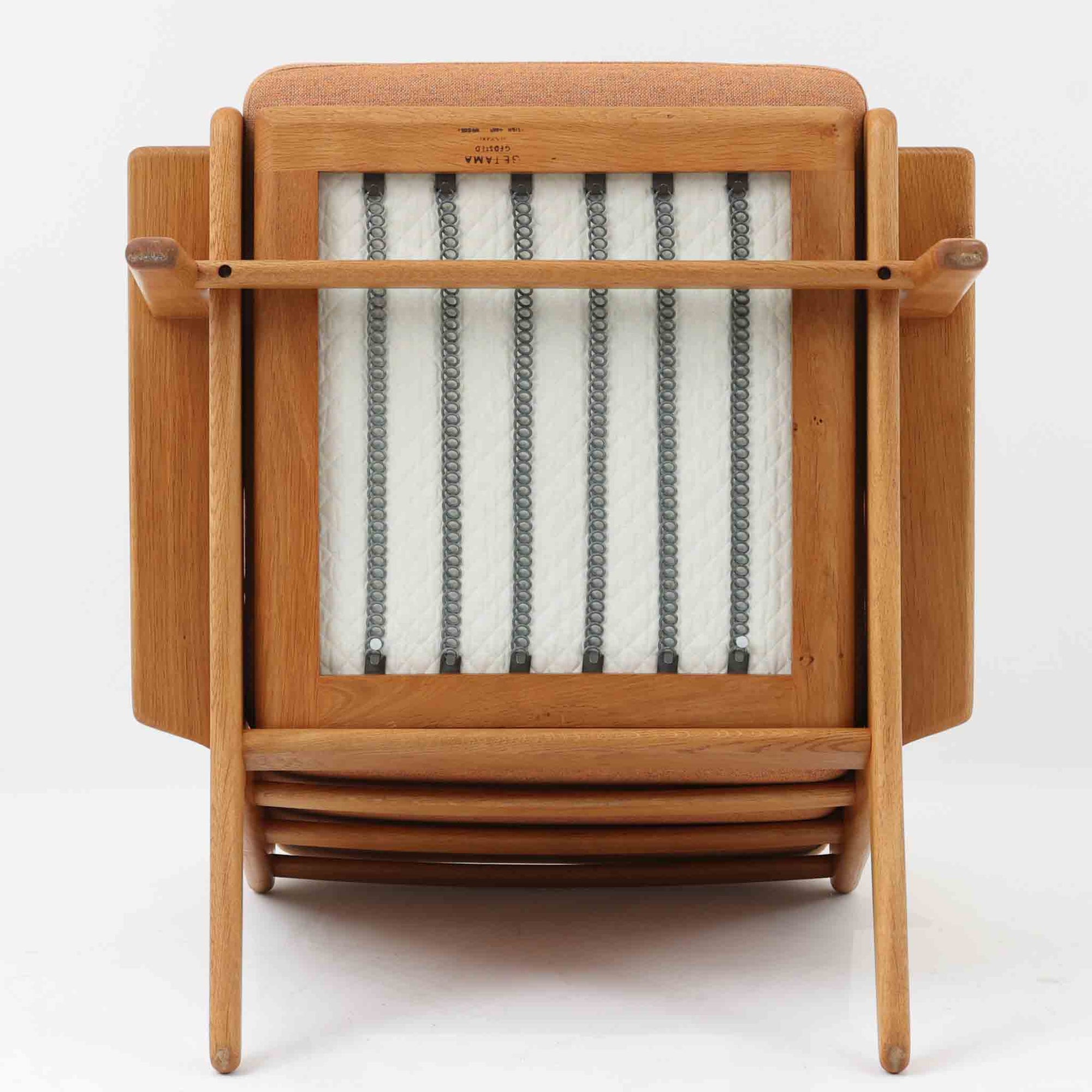 Hans J. Wegnerがデザインし、Getama社によって製作されたGE290は、構造の美しさと快適な座り心地を兼ね備えた北欧ビンテージを代表するシングルソファです。厚みのあるクッションと緩やかに傾斜した背もたれが身体を包み込み、自然と深いリラックス姿勢へと導きます。クッション内部にはビンテージ品ならではのスプリングが内包されており、しっかりとした弾力と安定感のある座り心地を生み出しています。オーク材のフレームは力強さと温かみを併せ持ち、アームから脚部にかけての造形にはウェグナーらしい彫刻的な魅力が感じられます。張地の落ち着いた色合いと、経年により深みを増した木部の表情が調和し、リビングや書斎で長く寄り添う一脚です。