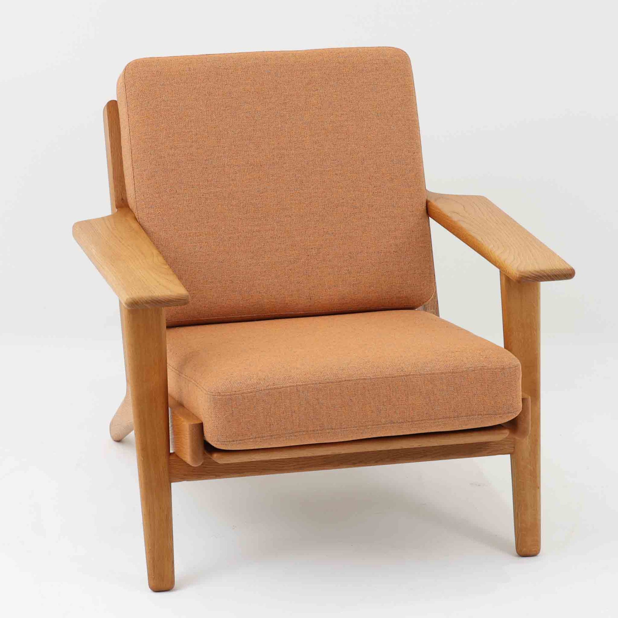 Hans J. Wegnerがデザインし、Getama社によって製作されたGE290は、構造の美しさと快適な座り心地を兼ね備えた北欧ビンテージを代表するシングルソファです。厚みのあるクッションと緩やかに傾斜した背もたれが身体を包み込み、自然と深いリラックス姿勢へと導きます。クッション内部にはビンテージ品ならではのスプリングが内包されており、しっかりとした弾力と安定感のある座り心地を生み出しています。オーク材のフレームは力強さと温かみを併せ持ち、アームから脚部にかけての造形にはウェグナーらしい彫刻的な魅力が感じられます。張地の落ち着いた色合いと、経年により深みを増した木部の表情が調和し、リビングや書斎で長く寄り添う一脚です。