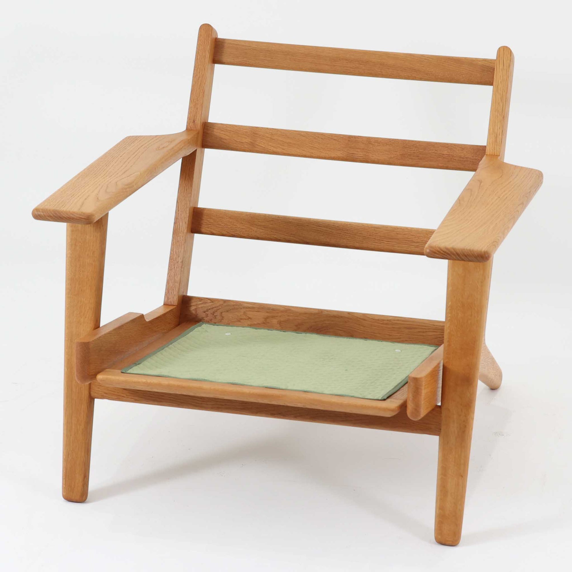 Hans J. Wegnerがデザインし、Getama社によって製作されたGE290は、構造の美しさと快適な座り心地を兼ね備えた北欧ビンテージを代表するシングルソファです。厚みのあるクッションと緩やかに傾斜した背もたれが身体を包み込み、自然と深いリラックス姿勢へと導きます。クッション内部にはビンテージ品ならではのスプリングが内包されており、しっかりとした弾力と安定感のある座り心地を生み出しています。オーク材のフレームは力強さと温かみを併せ持ち、アームから脚部にかけての造形にはウェグナーらしい彫刻的な魅力が感じられます。張地の落ち着いた色合いと、経年により深みを増した木部の表情が調和し、リビングや書斎で長く寄り添う一脚です。