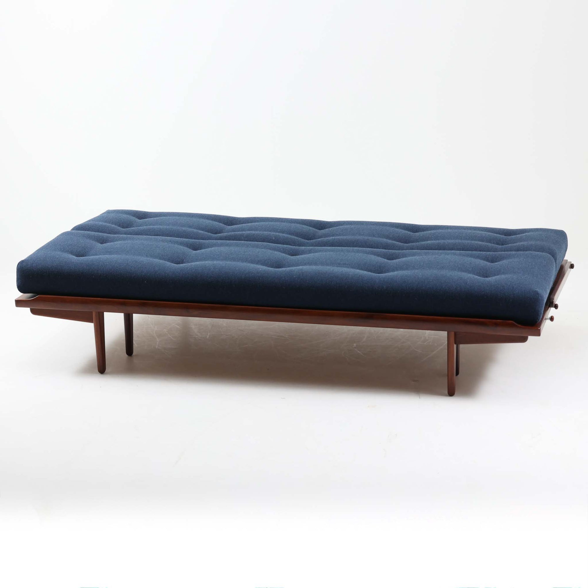 Poul M. Voltherによってデザインされたデイベッドは、機能性と美しさを兼ね備えたビンテージ家具です。ソファとしての使用はもちろん、背もたれを倒すことでリラックスできるベッドとしても使用でき、用途に応じて柔軟に活躍します。フレームにはアフロモシア材が使用されており、深みのある木目と上質な質感が空間に落ち着いた存在感を与えます。アフロモシア材仕様のモデルは流通数が少なく、希少性の高い点も魅力のひとつです。スラット構造による安定感のあるフレームに加え、クッション内部にはスプリングが内包されており、快適な座り心地と寝心地を提供してくれる一台です。