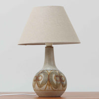 スーホルム・セラミック（Soholm Keramik）によるこちらのテーブルランプは、温かみのある陶磁器ベースに柔らかなブラウンとブルーで描かれた連続模様が印象的で、どこか手仕事の息づかいを感じさせる北欧ビンテージらしい魅力を備えています。丸みを帯びたベースからすっと伸びる首部のラインが美しく、リネンシェードを通した穏やかな灯りが空間にやさしい陰影を生み出します。高さ35cmと日常使いしやすいサイズで、ベッドサイドやリビングのサイドテーブルにも程よく収まり、落ち着いたインテリアに自然に馴染む一台です。