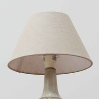 スーホルム・セラミック（Soholm Keramik）によるこちらのテーブルランプは、温かみのある陶磁器ベースに柔らかなブラウンとブルーで描かれた連続模様が印象的で、どこか手仕事の息づかいを感じさせる北欧ビンテージらしい魅力を備えています。丸みを帯びたベースからすっと伸びる首部のラインが美しく、リネンシェードを通した穏やかな灯りが空間にやさしい陰影を生み出します。高さ35cmと日常使いしやすいサイズで、ベッドサイドやリビングのサイドテーブルにも程よく収まり、落ち着いたインテリアに自然に馴染む一台です。