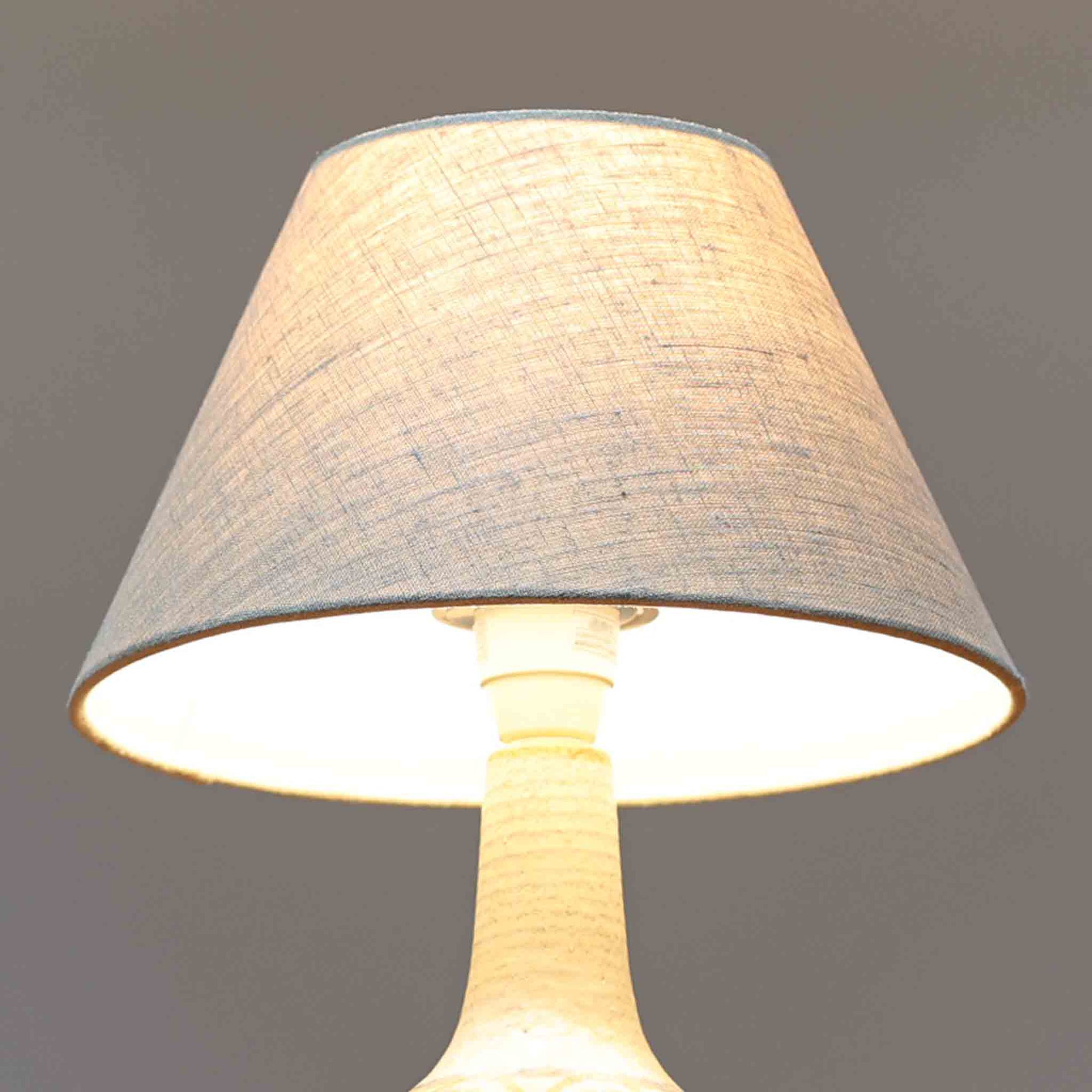 スーホルム・セラミック（Soholm Keramik）によるこちらのテーブルランプは、温かみのある陶磁器ベースに柔らかなブラウンとブルーで描かれた連続模様が印象的で、どこか手仕事の息づかいを感じさせる北欧ビンテージらしい魅力を備えています。丸みを帯びたベースからすっと伸びる首部のラインが美しく、リネンシェードを通した穏やかな灯りが空間にやさしい陰影を生み出します。高さ35cmと日常使いしやすいサイズで、ベッドサイドやリビングのサイドテーブルにも程よく収まり、落ち着いたインテリアに自然に馴染む一台です。