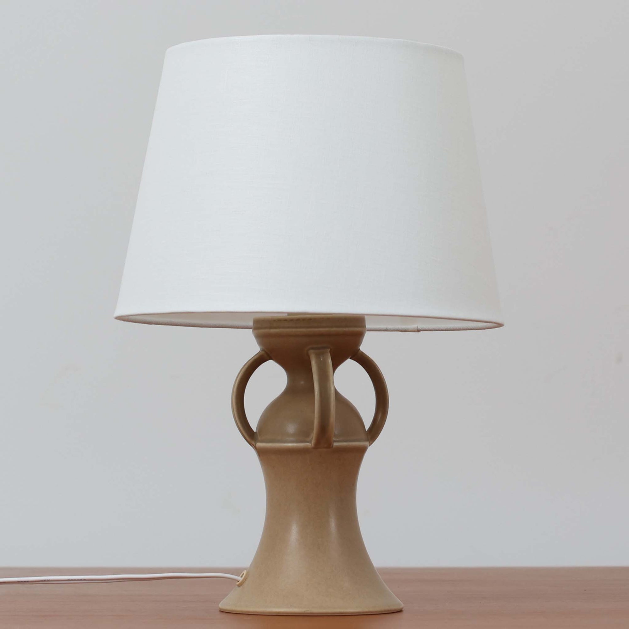 1993年にLe Klint創業50周年を記念して制作された、限定モデルのテーブルランプ「309」。ベースにはボーンホルム島の名門陶器工房Soholm（スーホルム）製のストーンウェアを採用し、シェードはLe Klint社製ではありませんが、新品のリネン製プリーツシェードを合わせており、クラシカルな佇まいと柔らかな光を演出します。北欧らしい温かみと洗練された存在感を持ち、ベッドサイドやリビングのアクセントとして取り入れやすい一灯です。ランプ底面には限定番号（No.0754）が刻まれており、コレクターズアイテムとしても価値ある一品です。