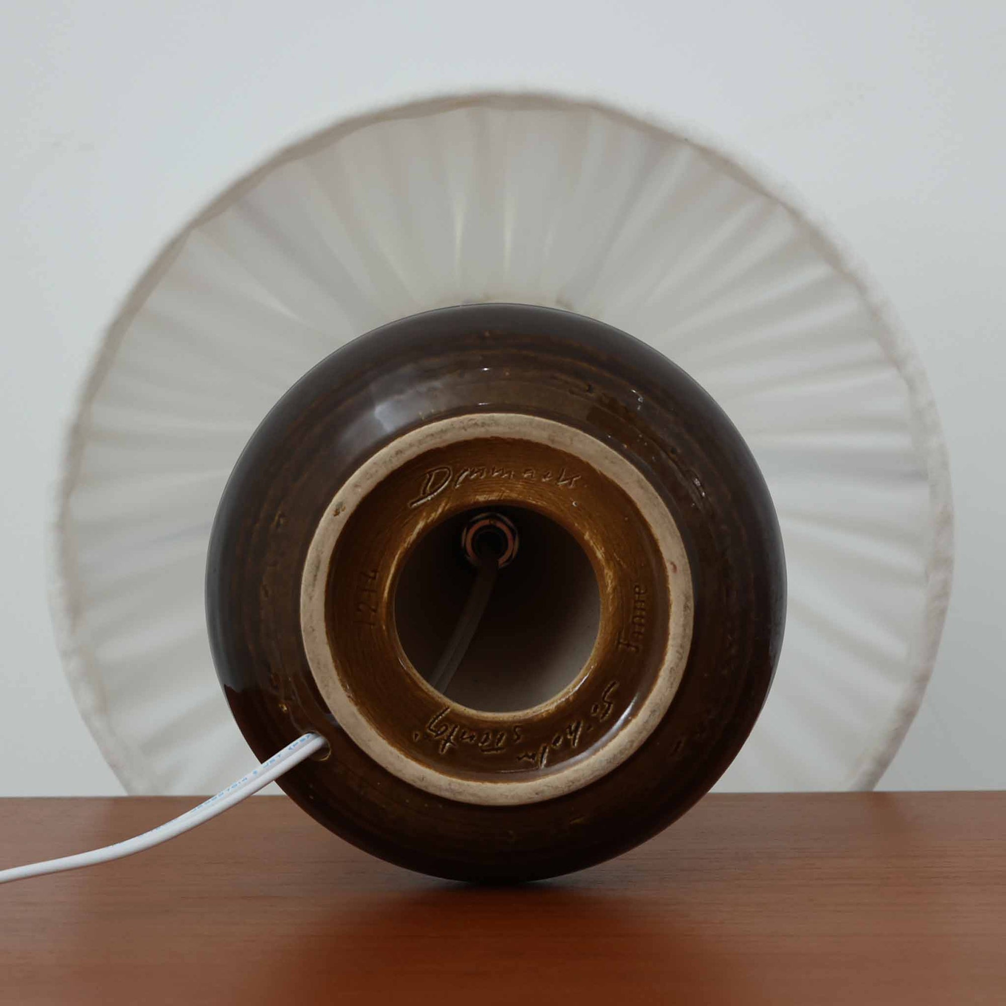 Soholm Keramik（スーホルム・セラミック）が手掛けたモデル1214のテーブルランプは、艶やかなブラウンの釉薬と段状のレリーフが生む豊かな表情が魅力で、陶磁器ならではの重量感と温かみが空間に落ち着いた存在感をもたらす北欧ビンテージ品です。柔らかな光を透過するリネンシェードがやさしい灯りを広げ、ベッドサイドやリビングのアクセント照明として取り入れやすく、経年の風合いが一層味わいを深めています。