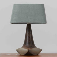 Michael Andersen & Sonが手掛けたこちらのテーブルランプは、陶磁器ならではの落ち着いた質感と、彫刻的に立ち上がるフォルムが存在感を放つ北欧ビンテージ品で、マットブラウンから生成り色へと移ろう釉薬のグラデーションが温かみある陰影を生み出し、リネンシェードを通したやわらかな灯りがベッドサイドやリビングに静かな安らぎを添えます。経年で深まった陶肌の表情がひとつとして同じものがない魅力となり、空間のアクセント照明として長くお楽しみいただける一台です。