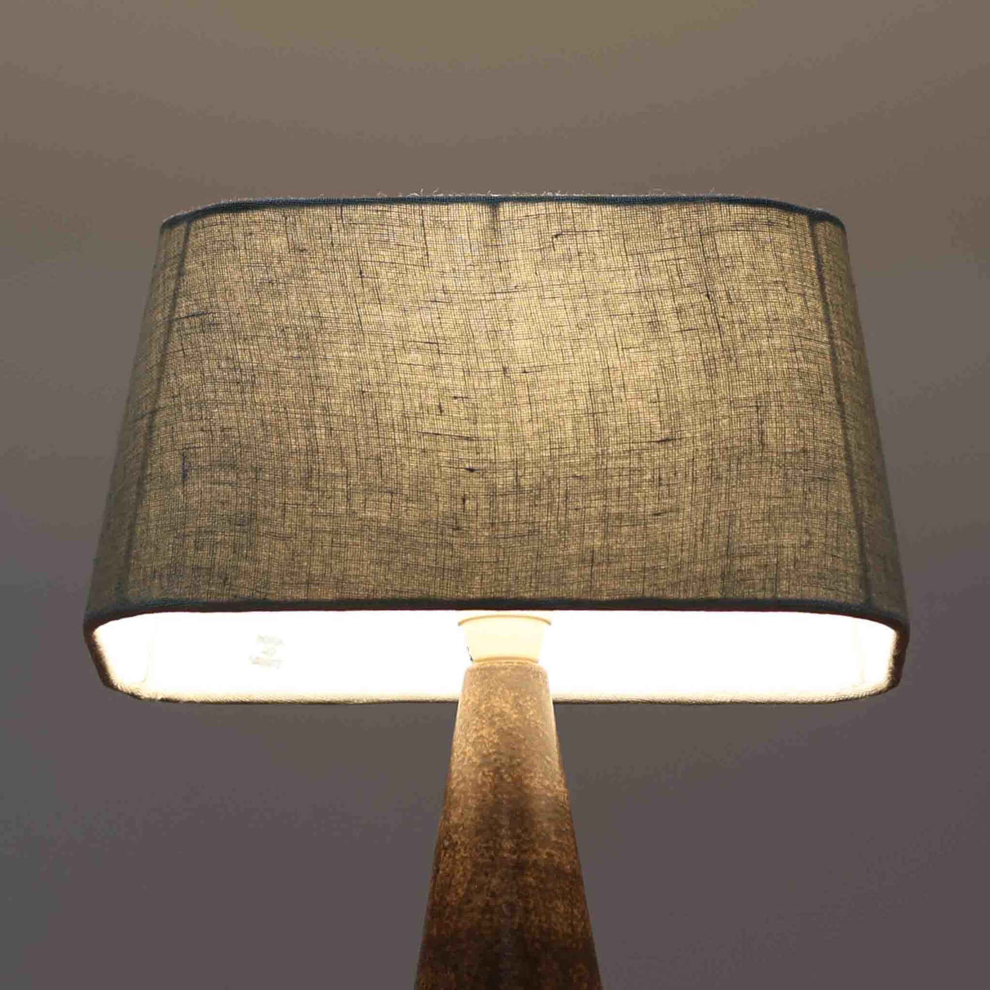 Michael Andersen &amp; Sonが手掛けたこちらのテーブルランプは、陶磁器ならではの落ち着いた質感と、彫刻的に立ち上がるフォルムが存在感を放つ北欧ビンテージ品で、マットブラウンから生成り色へと移ろう釉薬のグラデーションが温かみある陰影を生み出し、リネンシェードを通したやわらかな灯りがベッドサイドやリビングに静かな安らぎを添えます。経年で深まった陶肌の表情がひとつとして同じものがない魅力となり、空間のアクセント照明として長くお楽しみいただける一台です。