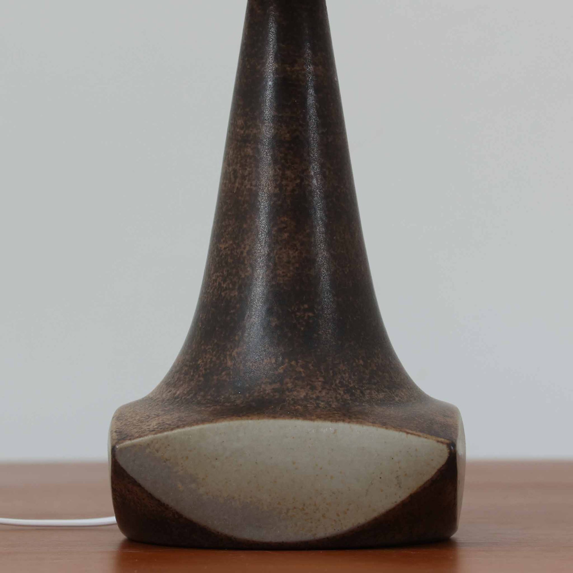 Michael Andersen &amp; Sonが手掛けたこちらのテーブルランプは、陶磁器ならではの落ち着いた質感と、彫刻的に立ち上がるフォルムが存在感を放つ北欧ビンテージ品で、マットブラウンから生成り色へと移ろう釉薬のグラデーションが温かみある陰影を生み出し、リネンシェードを通したやわらかな灯りがベッドサイドやリビングに静かな安らぎを添えます。経年で深まった陶肌の表情がひとつとして同じものがない魅力となり、空間のアクセント照明として長くお楽しみいただける一台です。