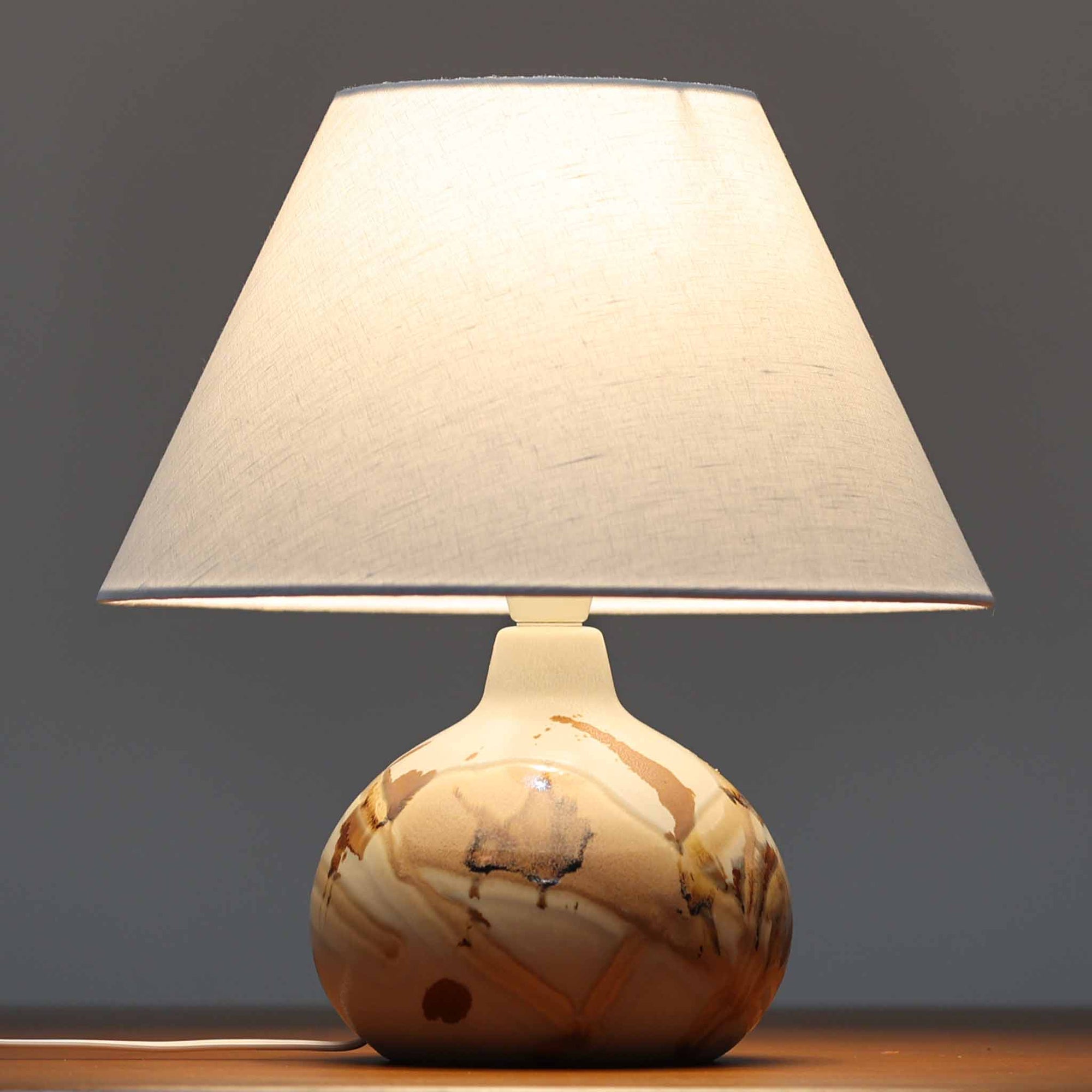 Soholm Keramik（スーホルム・セラミック）が手掛けたこちらのテーブルランプは、淡いグレーを基調にブラウンの流れるような釉薬模様が美しく広がる有機的な表情が魅力で、丸みを帯びた陶磁器のベースが空間にやさしい存在感をもたらす北欧ビンテージ品です。リネンシェードを透ける柔らかな灯りが落ち着いた雰囲気をつくり、ベッドサイドやリビングの間接照明として取り入れやすく、経年によって深まった色合いと一点物ならではの味わいを長く楽しめる一台です。