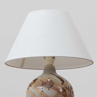 Soholm Keramik（スーホルム・セラミック）が手掛けたこちらのテーブルランプは、淡いグレーを基調にブラウンの流れるような釉薬模様が美しく広がる有機的な表情が魅力で、丸みを帯びた陶磁器のベースが空間にやさしい存在感をもたらす北欧ビンテージ品です。リネンシェードを透ける柔らかな灯りが落ち着いた雰囲気をつくり、ベッドサイドやリビングの間接照明として取り入れやすく、経年によって深まった色合いと一点物ならではの味わいを長く楽しめる一台です。