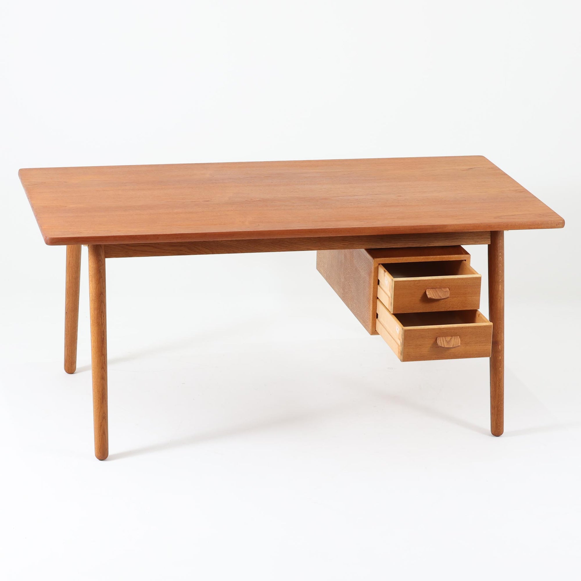 Poul M. Voltherがデザインし、FDB Moblerによって製作された片袖デスク。チーク材の天板と収納部、オーク材の脚部を組み合わせた構成に、真鍮の金具がさりげないアクセントを添える北欧ビンテージらしい一台です。幅160cmのゆとりあるサイズ感に対して、脚部や幕板は軽やかに設計されており、空間に圧迫感を与えません。片側に備えた引き出しユニットは、取り付けた状態でもスライドさせて位置調整が可能で、左右どちら側にも付け替えられる柔軟な構造となっています。さらに引き出しを取り外すことで、デスクとしてだけでなくダイニングテーブルとしても使用でき、暮らしの変化に合わせた使い方ができる点も魅力です。素材ごとの質感の違いと、経年により深みを増した木肌の表情が調和した、長く使い続けたくなるデザインです。
