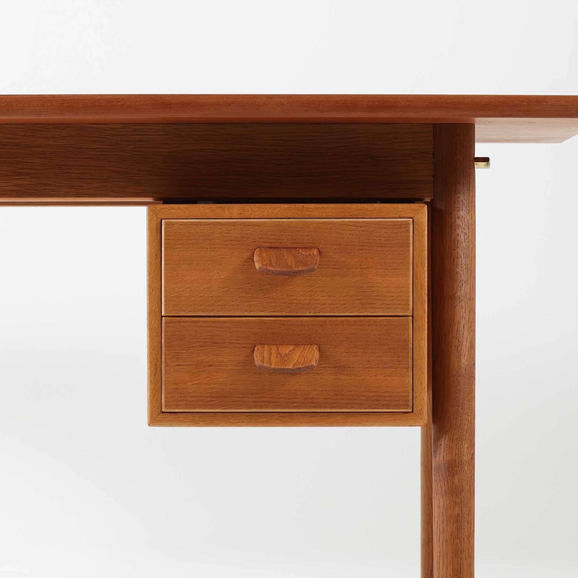 Poul M. Voltherがデザインし、FDB Moblerによって製作された片袖デスク。チーク材の天板と収納部、オーク材の脚部を組み合わせた構成に、真鍮の金具がさりげないアクセントを添える北欧ビンテージらしい一台です。幅160cmのゆとりあるサイズ感に対して、脚部や幕板は軽やかに設計されており、空間に圧迫感を与えません。片側に備えた引き出しユニットは、取り付けた状態でもスライドさせて位置調整が可能で、左右どちら側にも付け替えられる柔軟な構造となっています。さらに引き出しを取り外すことで、デスクとしてだけでなくダイニングテーブルとしても使用でき、暮らしの変化に合わせた使い方ができる点も魅力です。素材ごとの質感の違いと、経年により深みを増した木肌の表情が調和した、長く使い続けたくなるデザインです。
